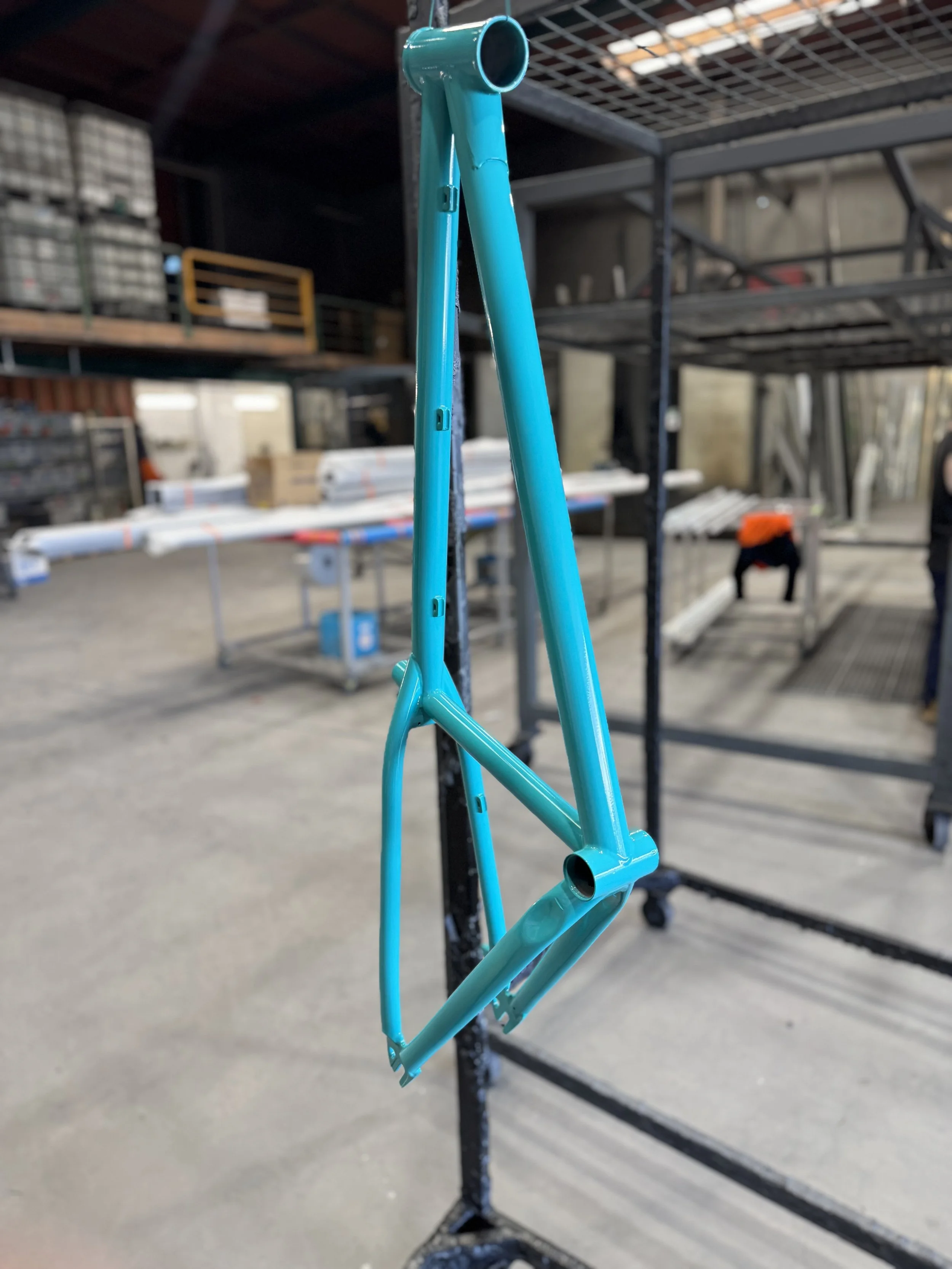A turquoise mountain bike frame hanging on a black metal display rack inside a warehouse or hardware store.