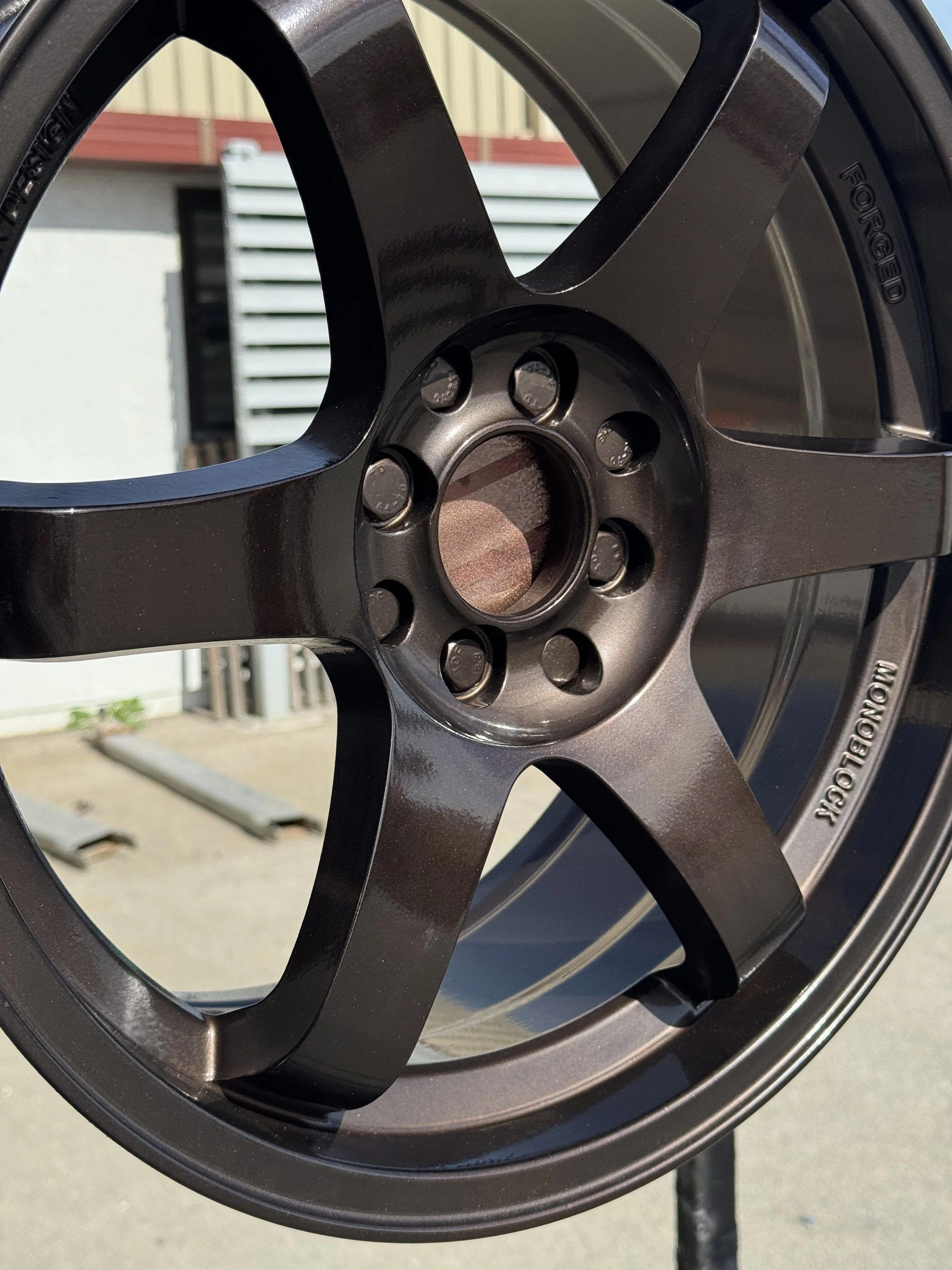 Close-up of a black alloy wheel rim with visible lug nut holes and the imprint 'FORGED'.