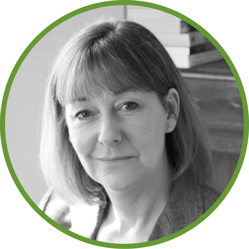 Dr Adrienne photo with shoulder-length hair, wearing a suit jacket, with books in the background.