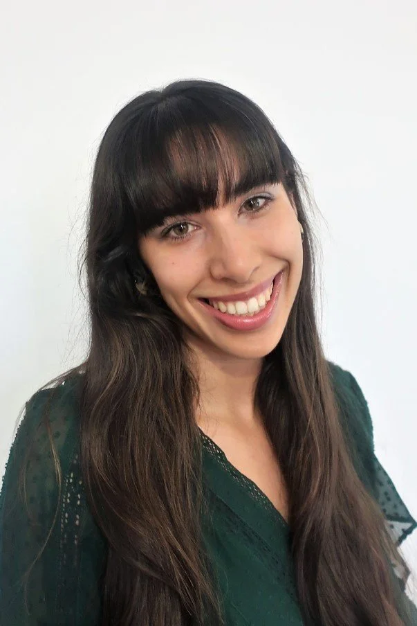 Mulher com cabelo comprido e franja, vestindo blusa verde, sorrindo para a câmera com fundo branco.