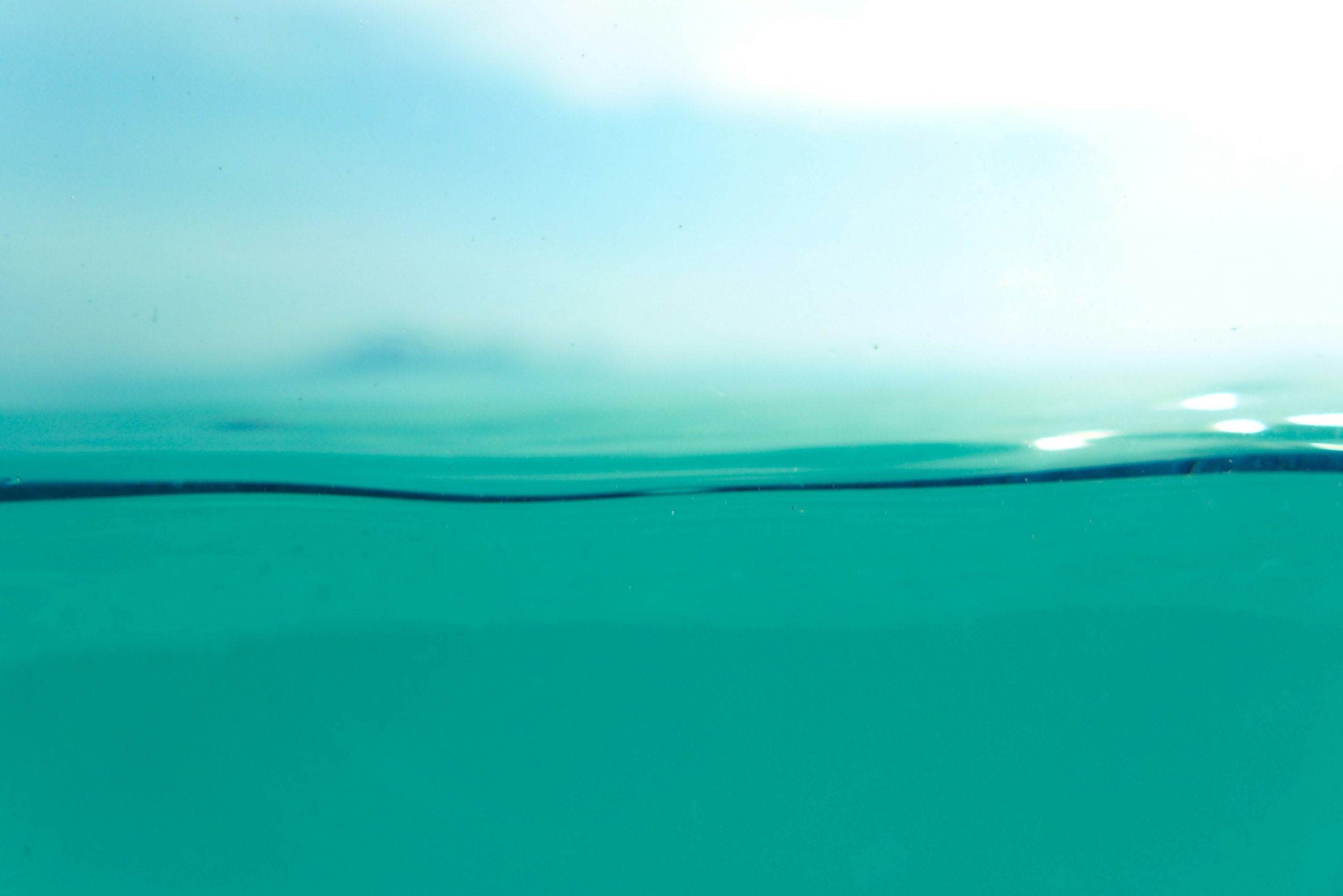Underwater view of the ocean surface with a horizon line and a partly cloudy sky.