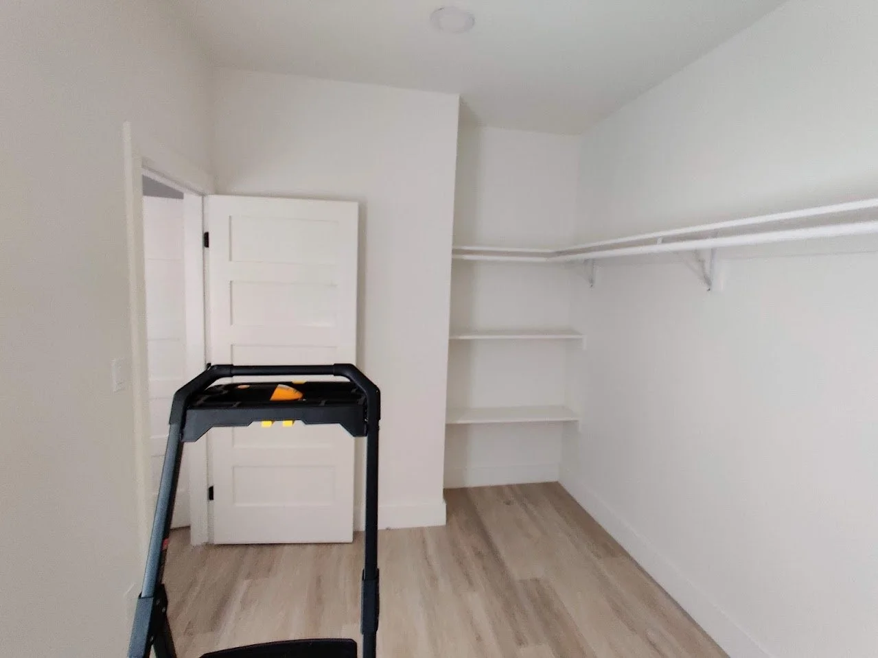 Empty walk-in closet with white walls, light wood flooring, shelves, and hanging rods.
