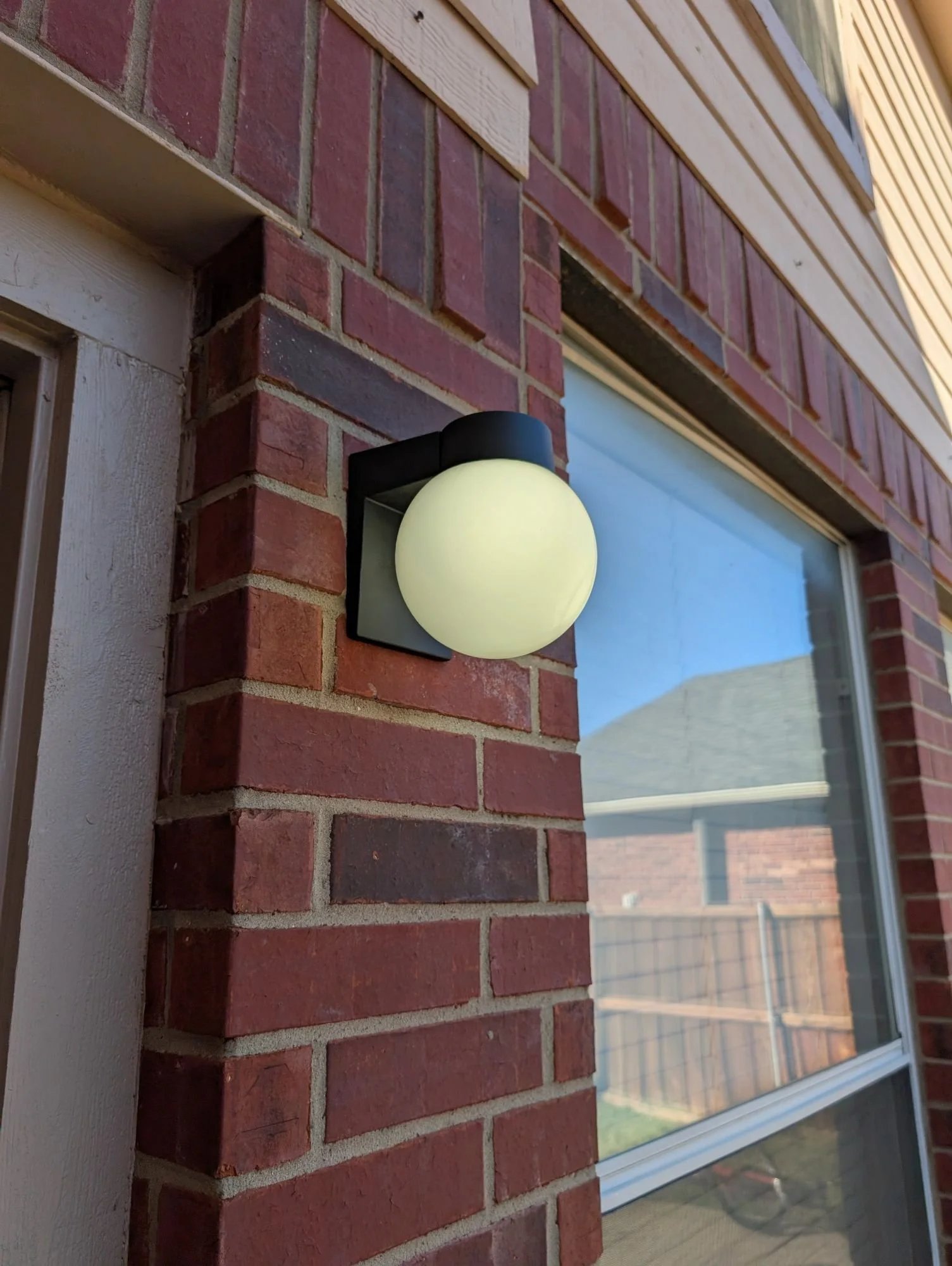 Exterior wall with a round light fixture attached to red brick, near a window.