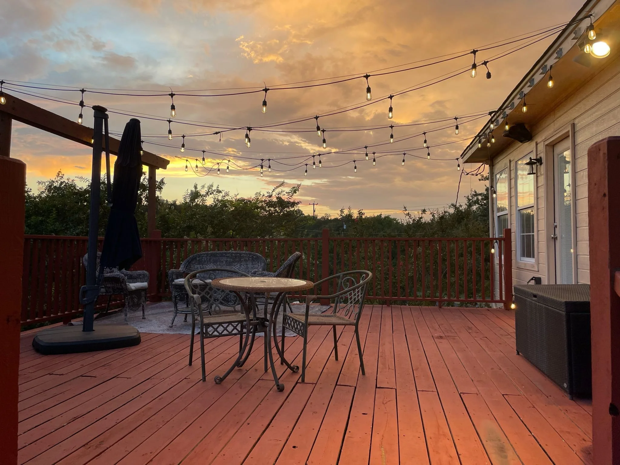 Outdoor wooden deck with patio furniture, string lights, and a sunset sky.