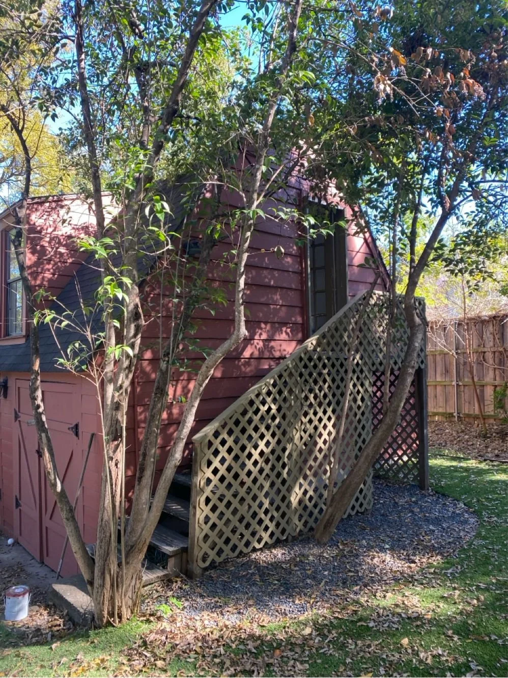 Small wooden shed with stairs and lattice, surrounded by trees and dappled sunlight.