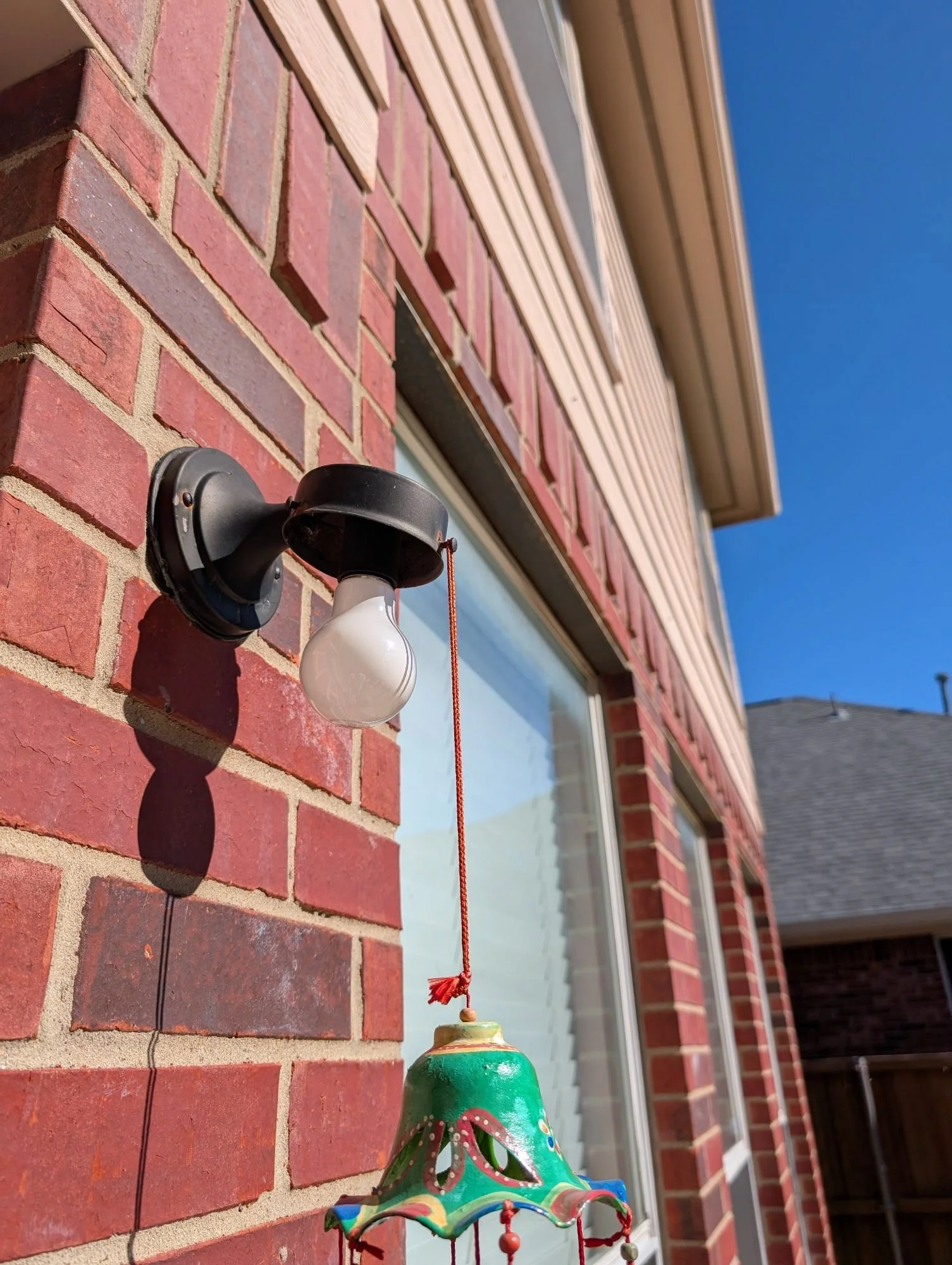 Close-up of a red brick exterior wall with a light fixture and a colorful hanging decoration.