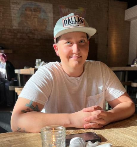 Person wearing a "Dallas" cap and white shirt sitting at a table in a restaurant with rustic decor.
