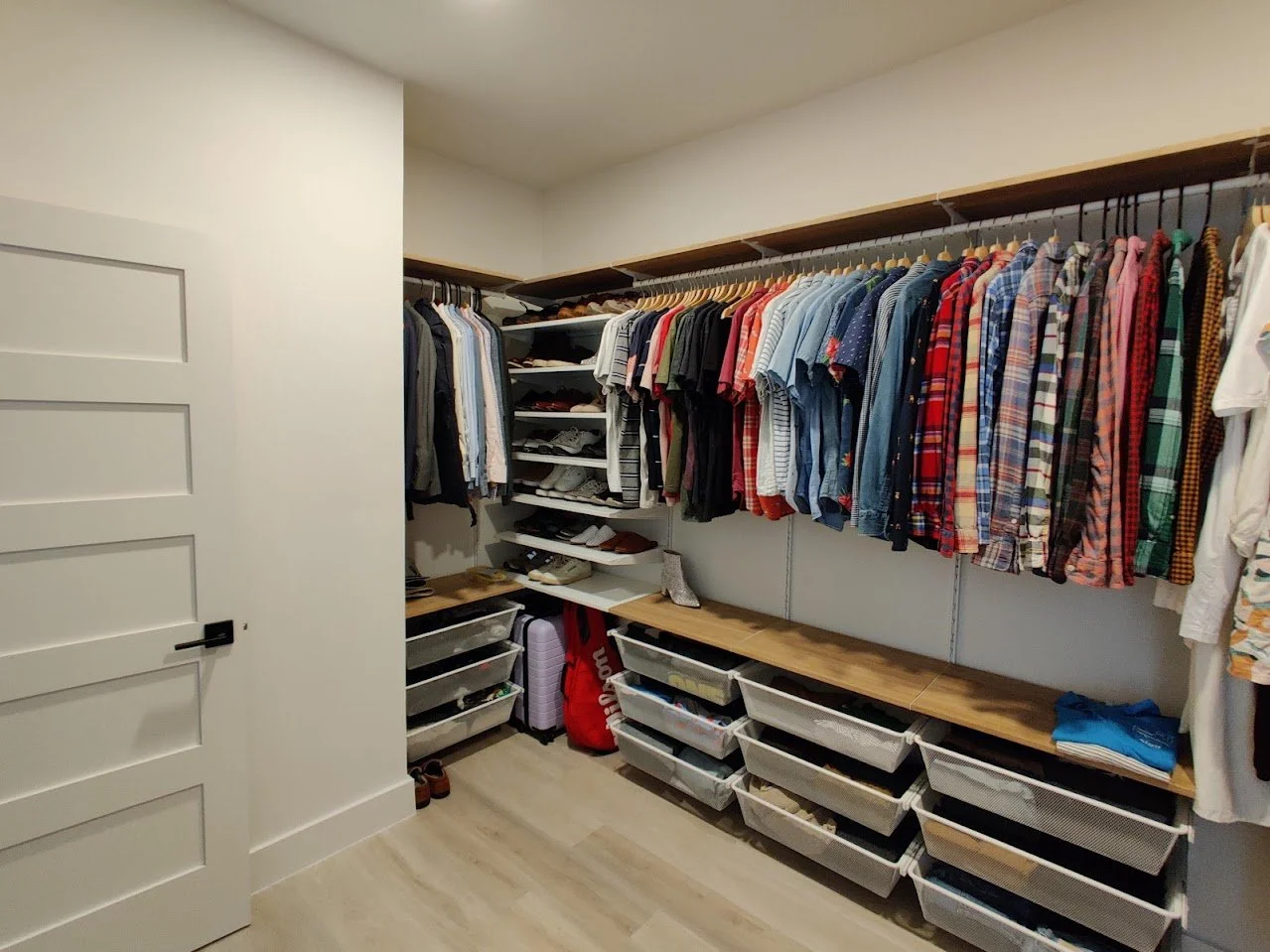 Walk-in closet with clothes hanging neatly on racks, assorted shirts in various colors and patterns, shelves holding shoes, and storage bins underneath.