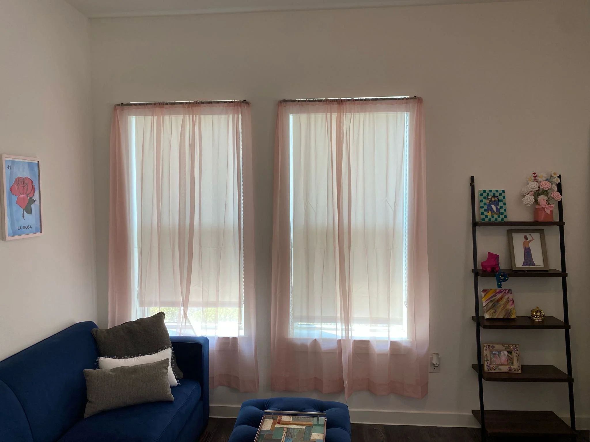 Room with blue sofa, pink curtains, and wall shelf