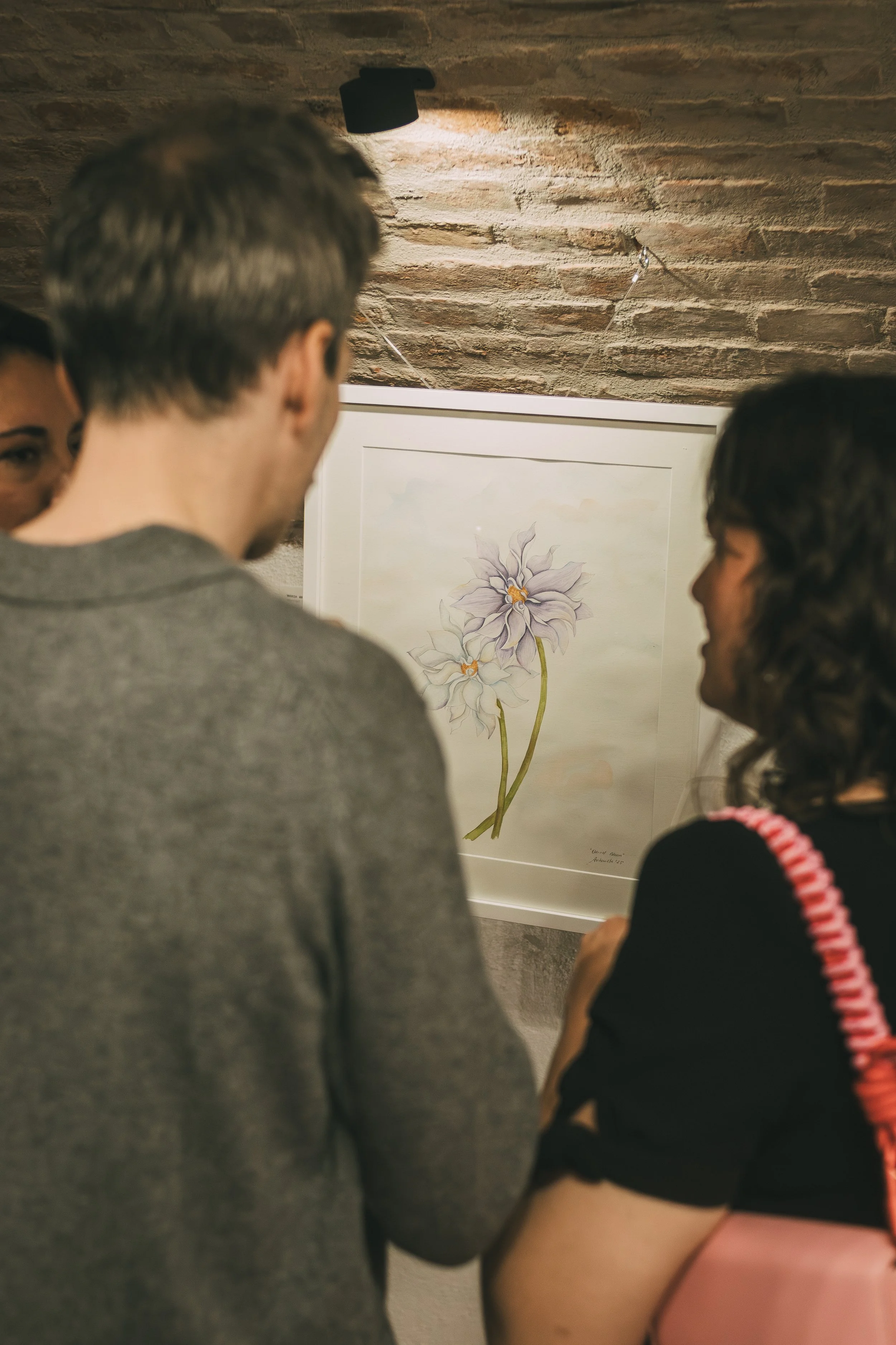 Three people looking at a framed watercolor painting of two purple flowers with yellow centers in an art gallery.