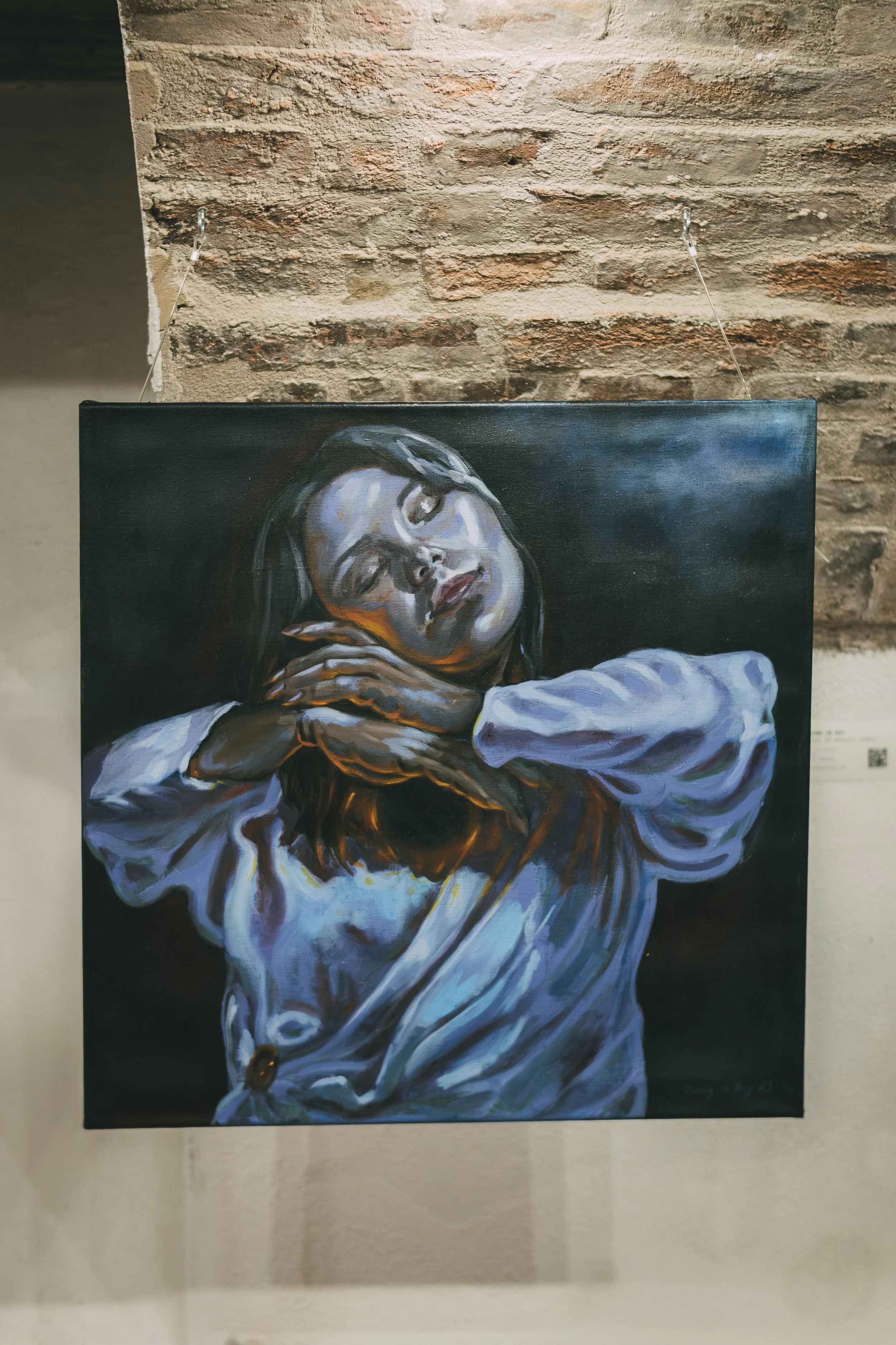 Painting of a woman with closed eyes, resting her head on her arms, with dark hair and dark background.