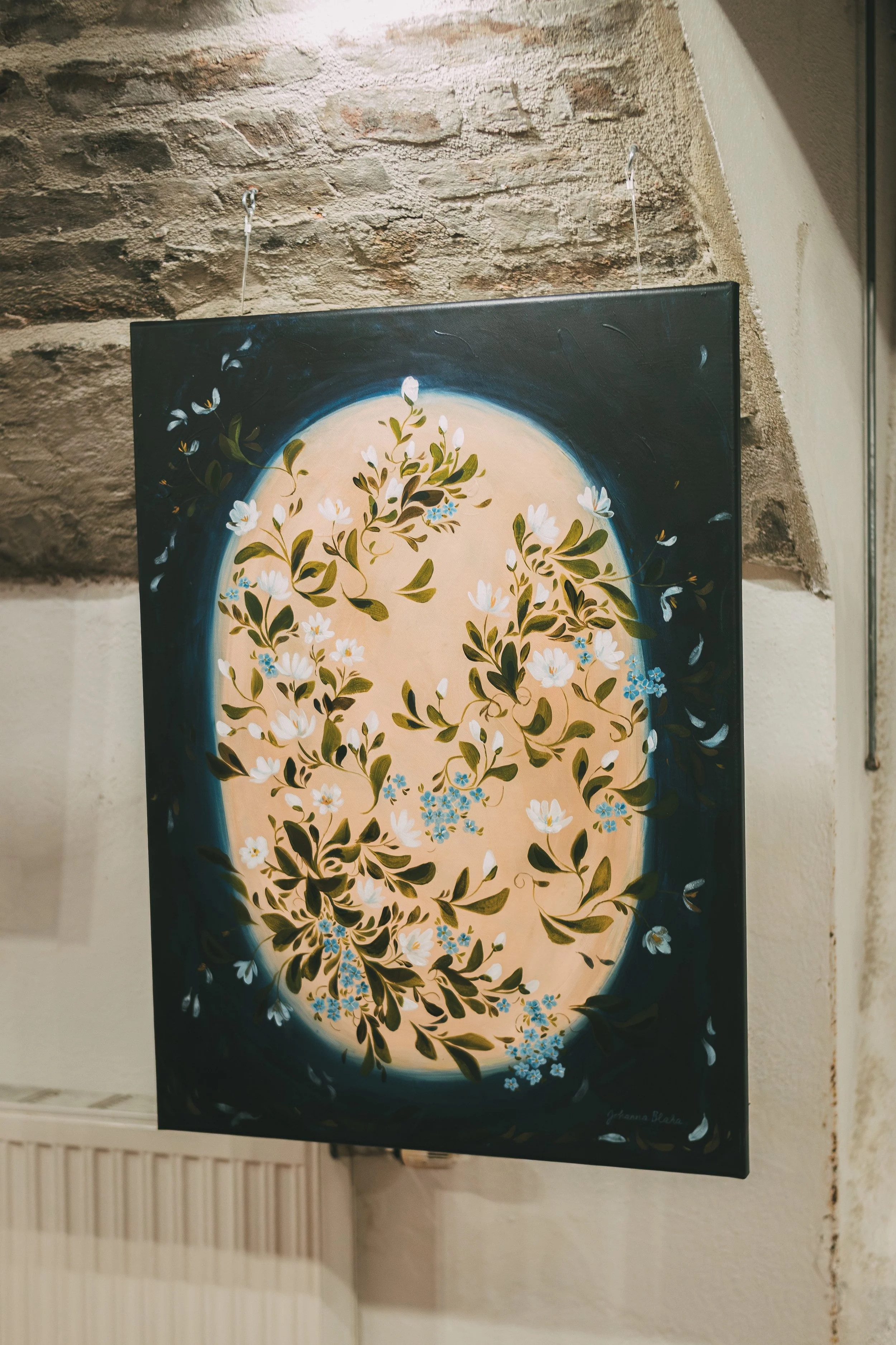 Painting of a full moon with white flowers and green leaves against a dark background, signed by Gianna Becha.