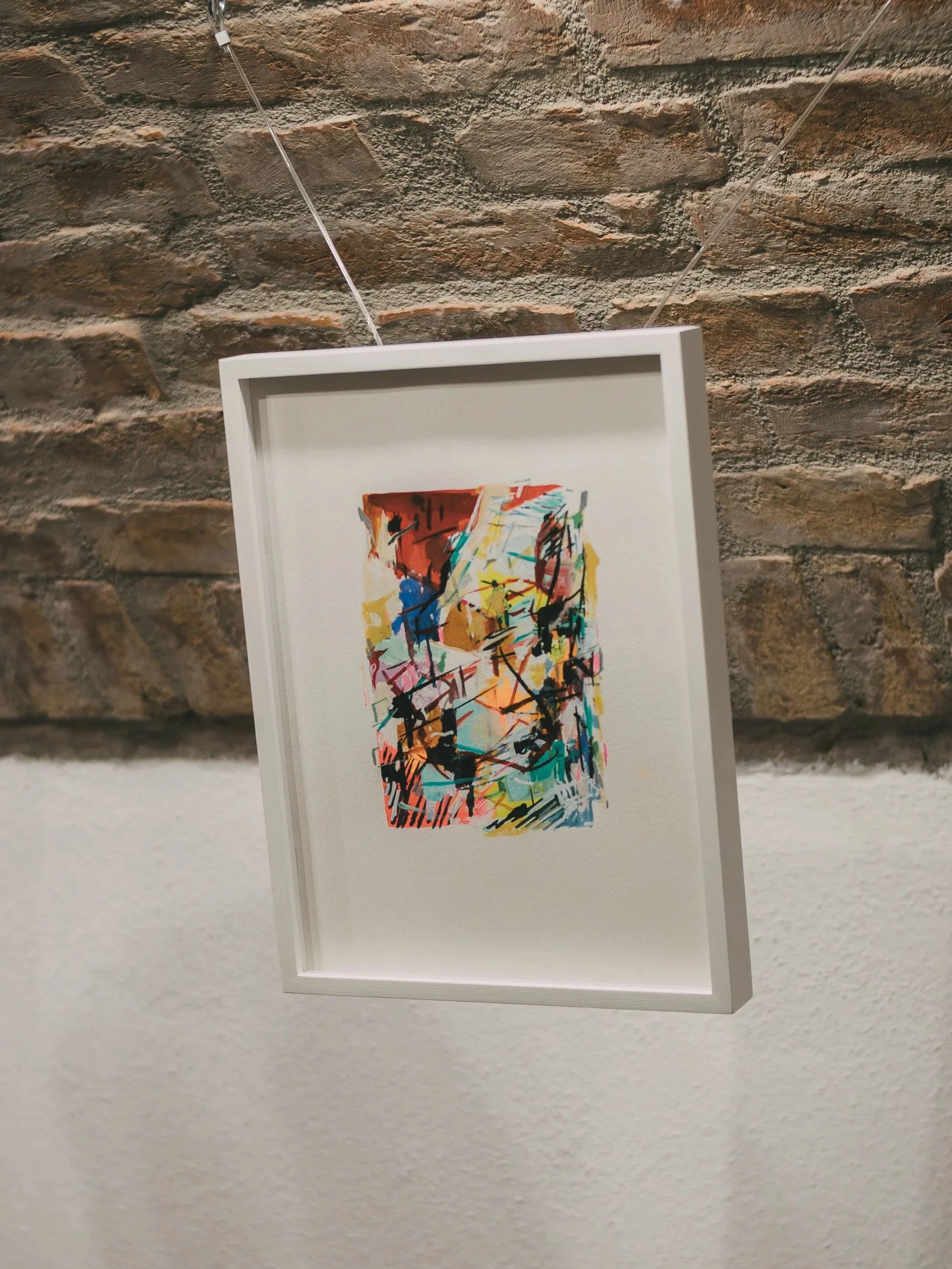 Abstract colorful art piece hanging on a wire against a brick wall.