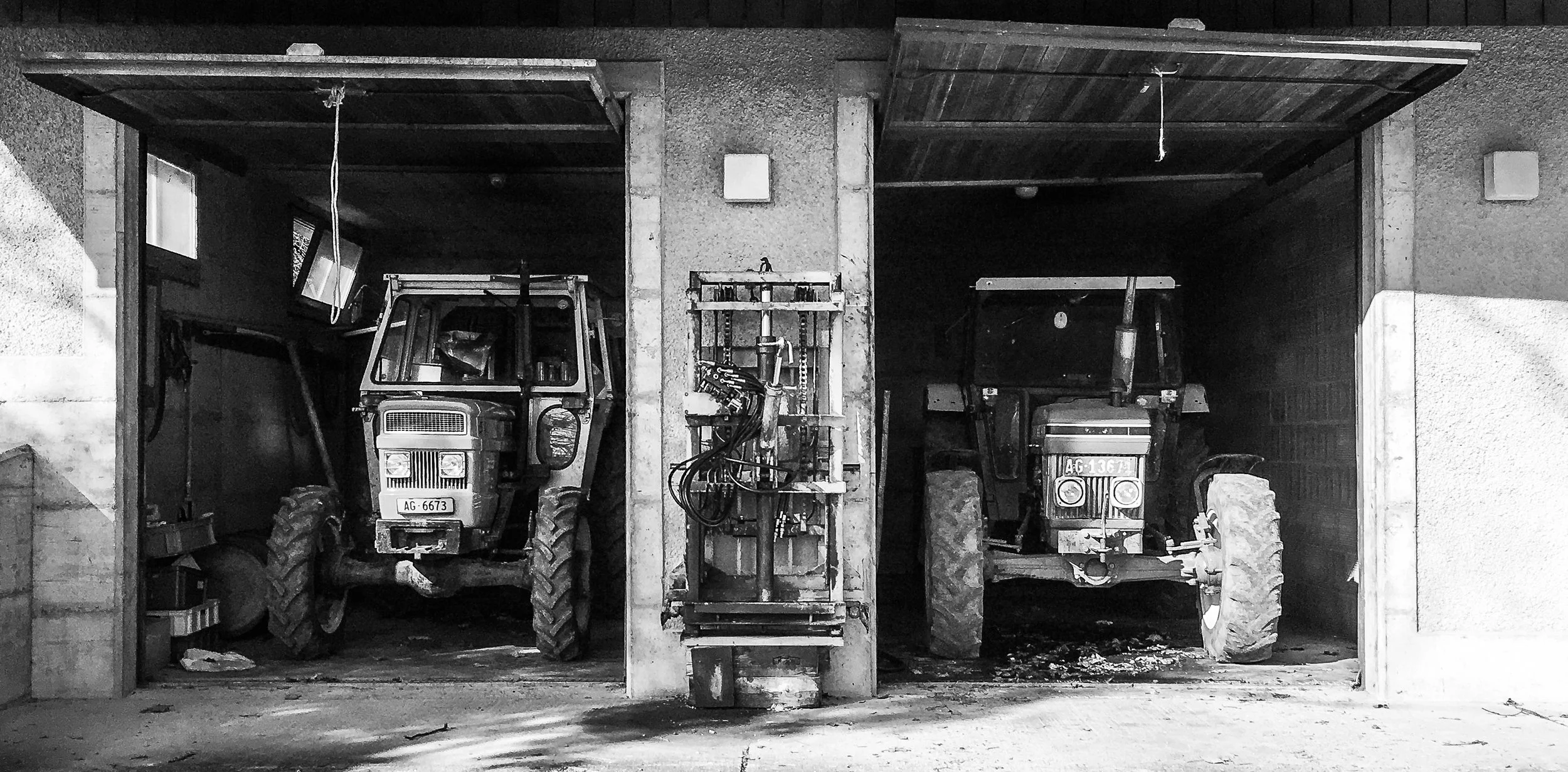 Black and white photograph of two tractors in a garage