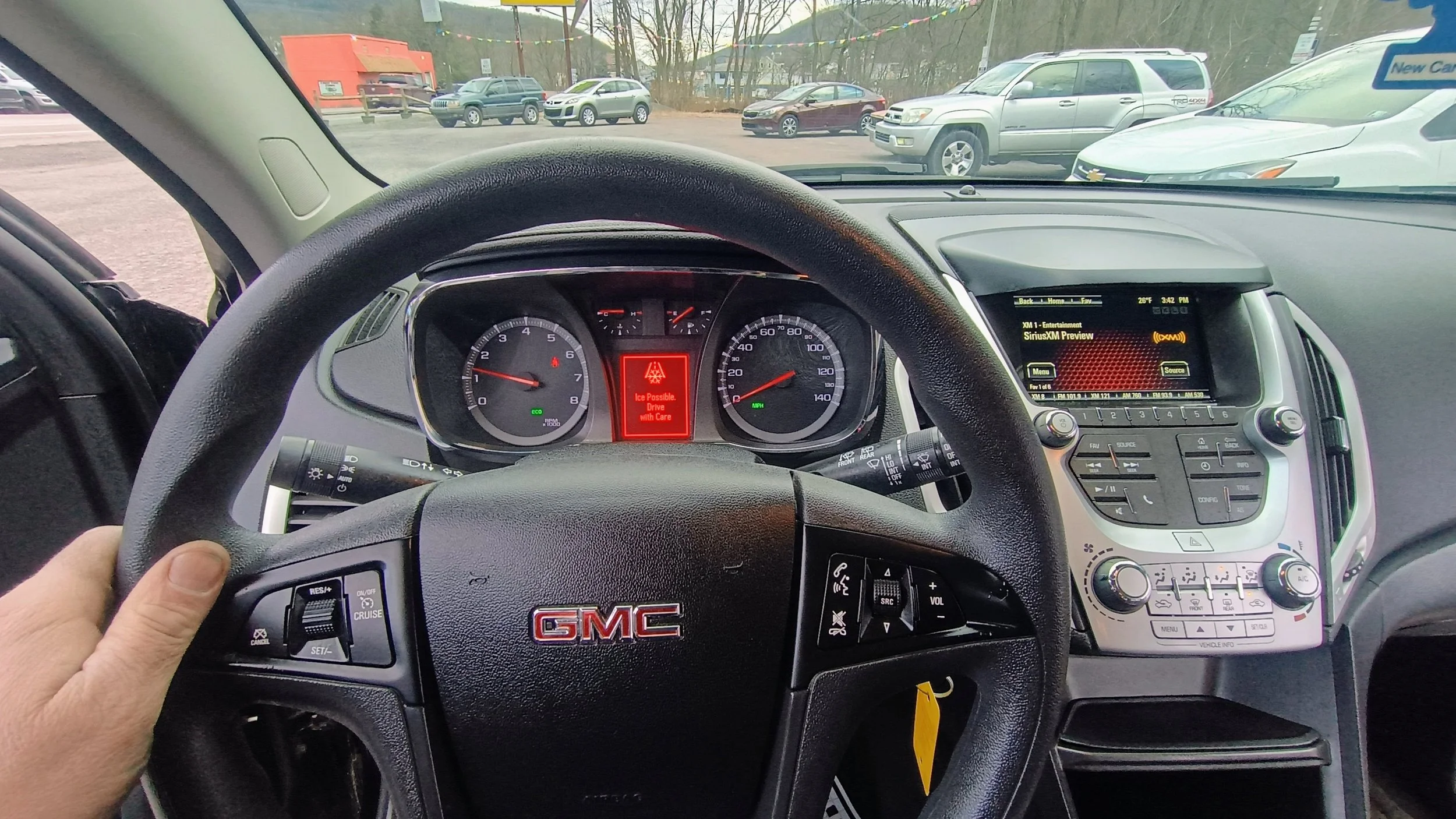 Inside view of a GMC vehicle showing the steering wheel, dashboard, and center console with an infotainment screen. The dashboard displays a warning light and message indicating icy conditions.