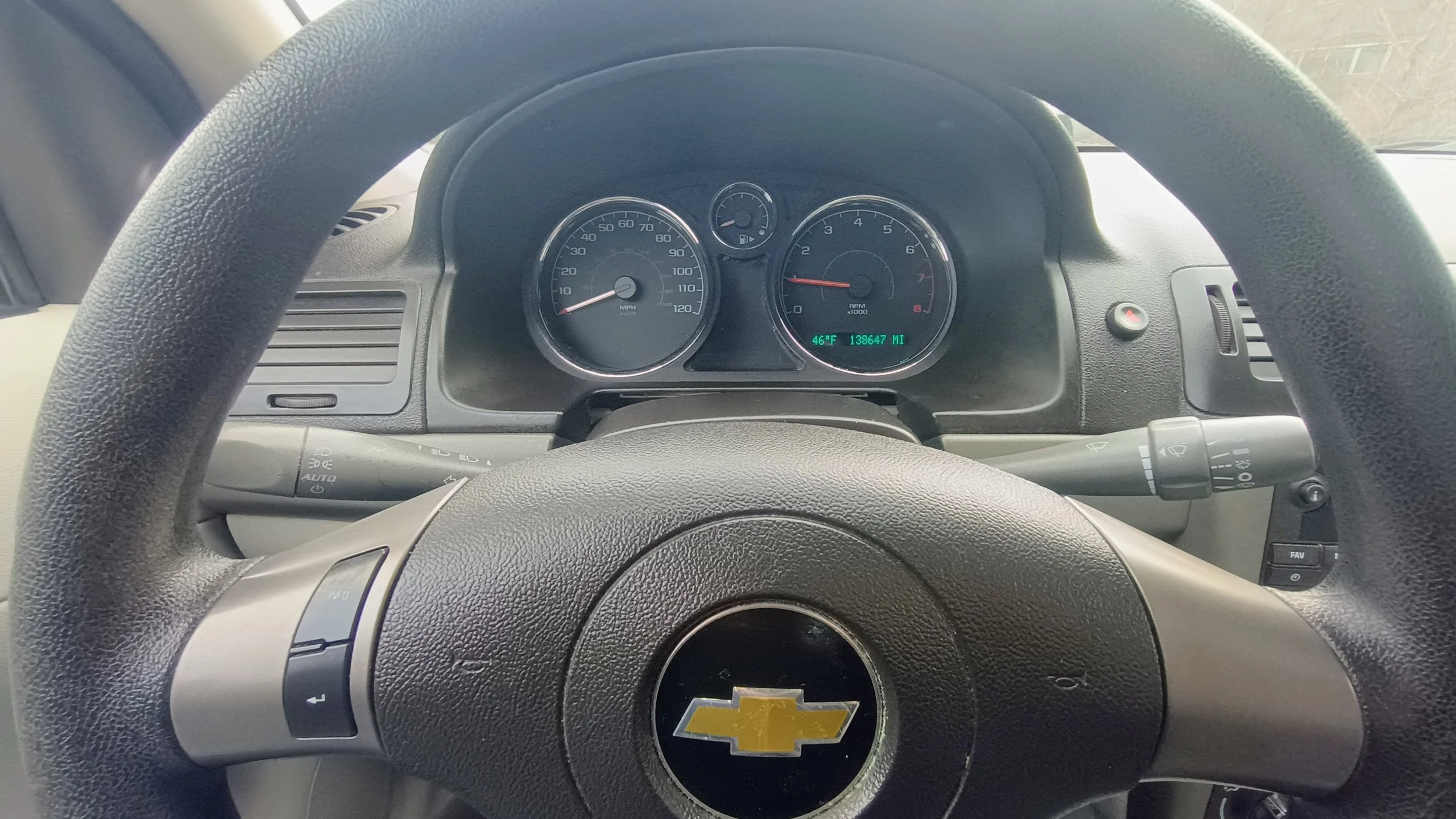 The image shows the interior dashboard of a Chevrolet vehicle, featuring a steering wheel with the Chevrolet emblem, and analog gauges including a speedometer, tachometer, fuel gauge, and temperature gauge, with a digital display indicating the temperature and odometer reading.