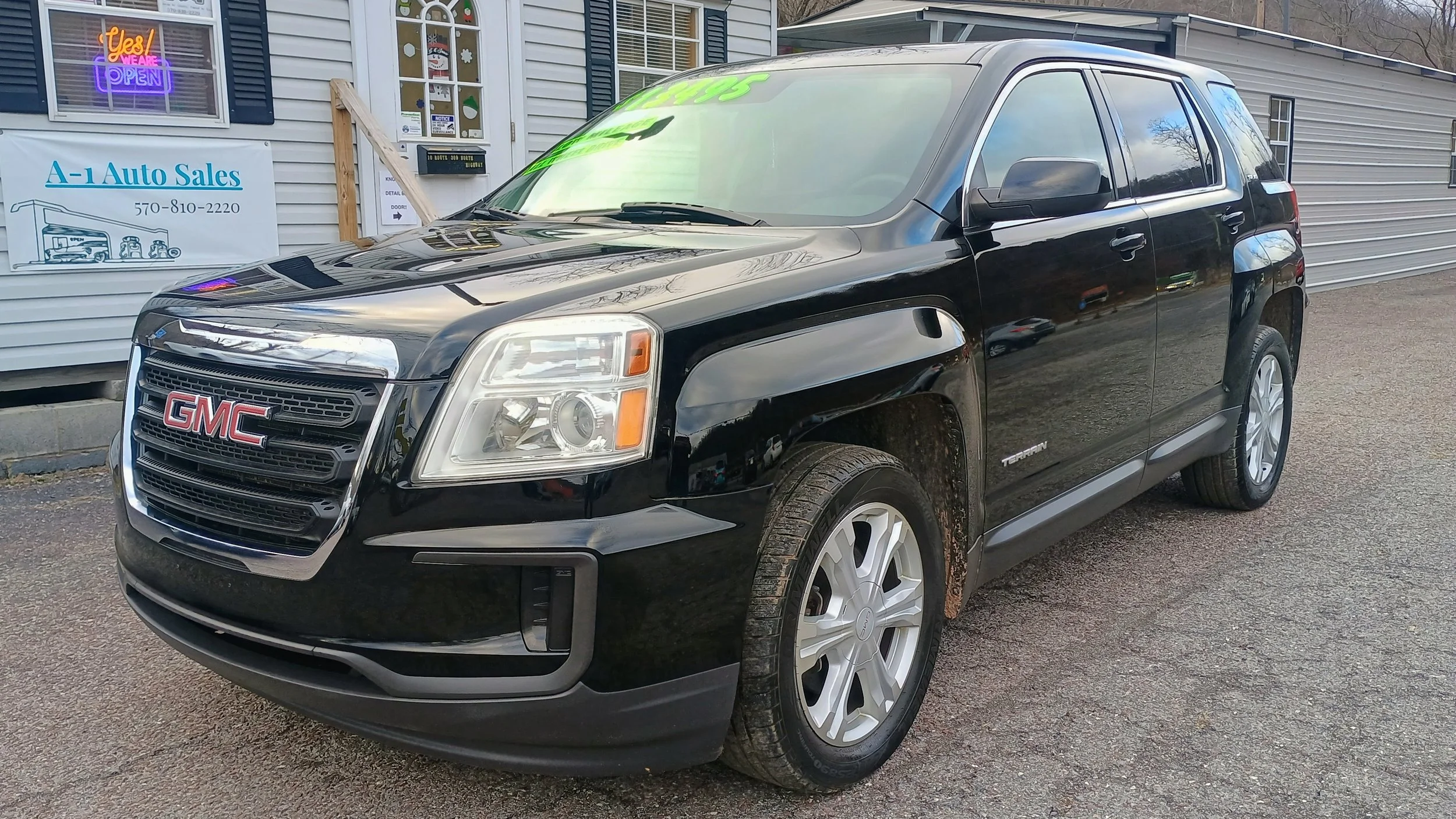 Black GMC Terrain SUV parked outside a building with a sign that reads A-1 Auto Sales and a neon open sign in the window.