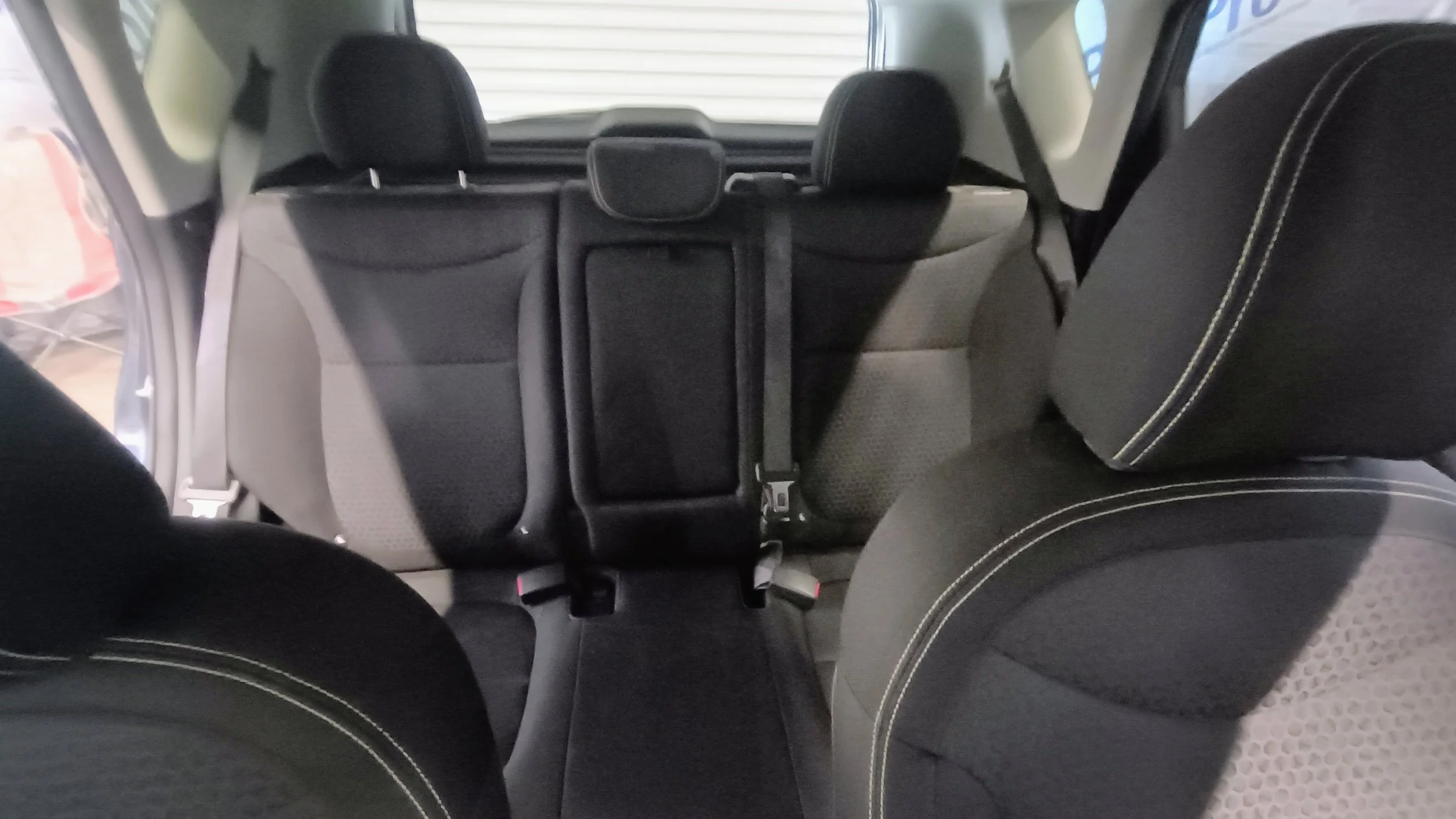 Interior of a vehicle showing three rows of seats with black upholstery. The view is from the back, facing the front windshield, with the headrest of the third-row seats visible in the background.