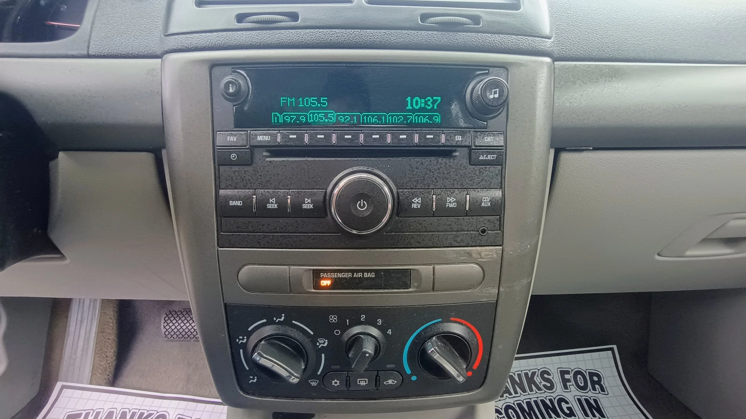 The car's dashboard features an audio system displaying the radio station FM 105.5 and the time 10:37. Below, there are climate controls including temperature, fan speed, and airflow direction dials.