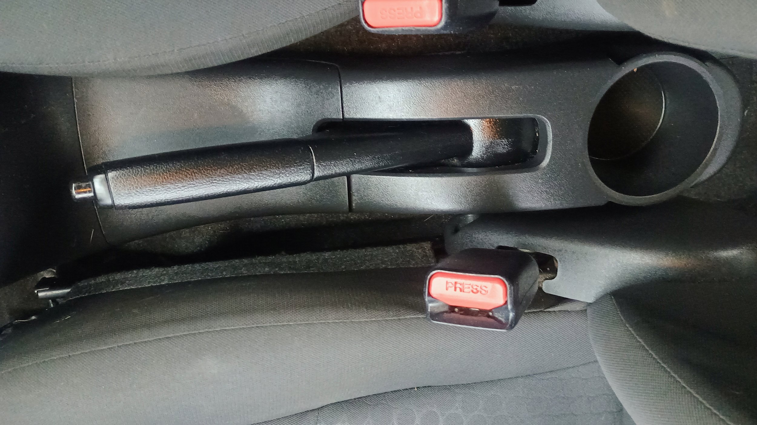 Center console of a car showing the handbrake, a USB port, and seatbelt release buttons labeled 'PRESS'.