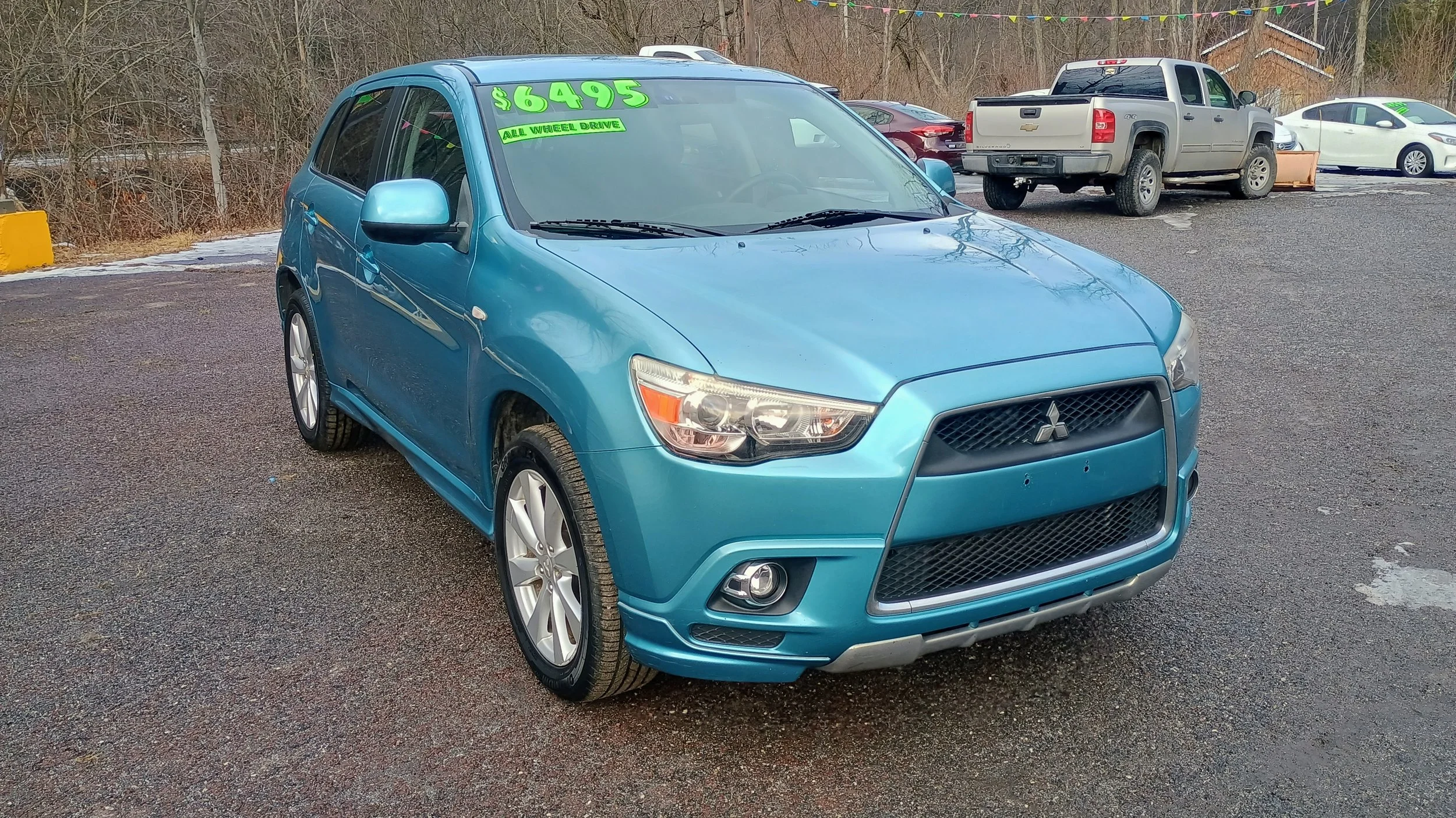 Blue Mitsubishi car for sale at a used car dealership with a price of $6495 displayed on the windshield.