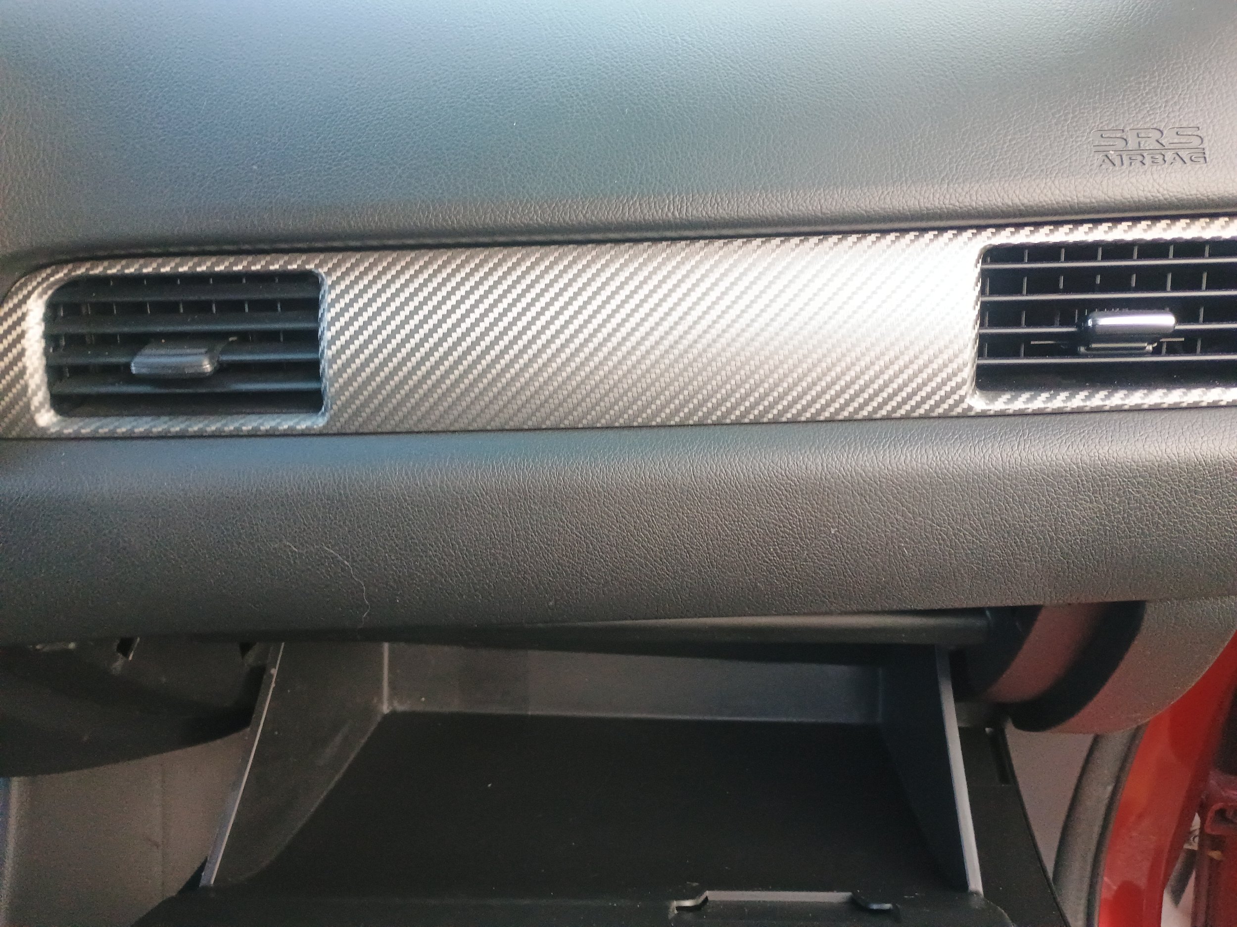 Close-up of a car dashboard with two air vents and a textured panel in between, labeled with the SRS Airbag logo.