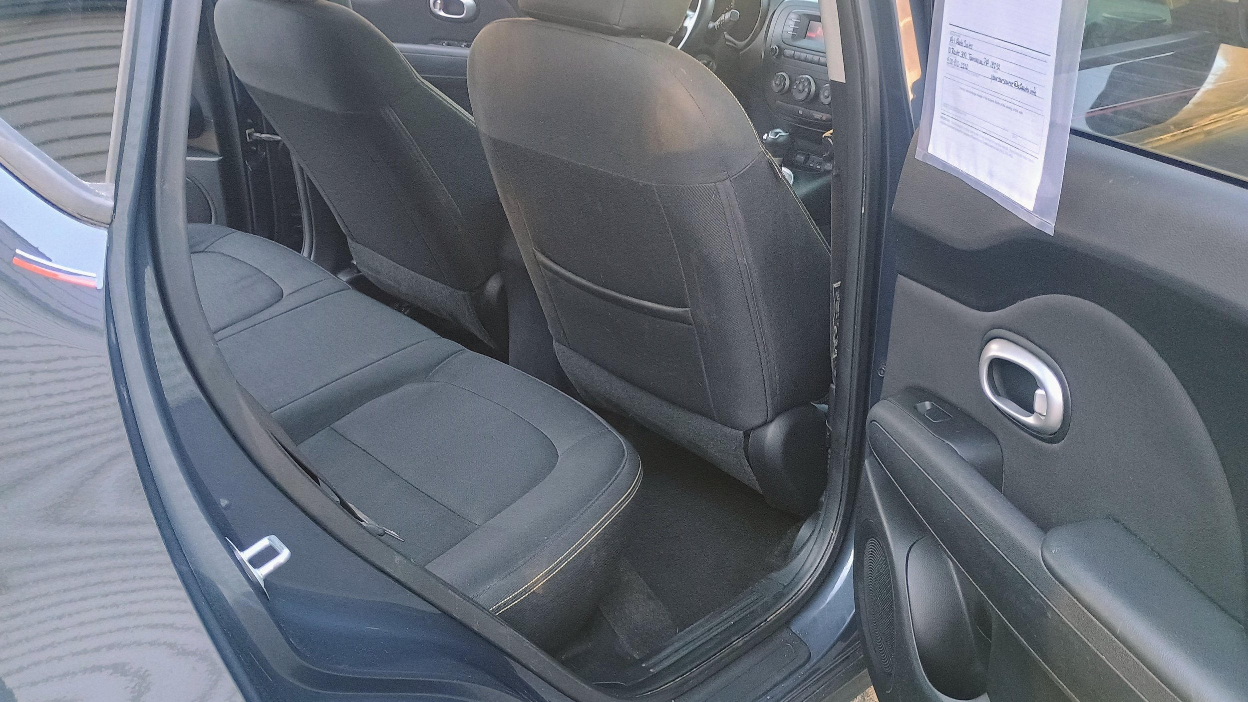 Interior view of a compact car, showing the backseat area with black seats, a front dashboard, and the front seats.