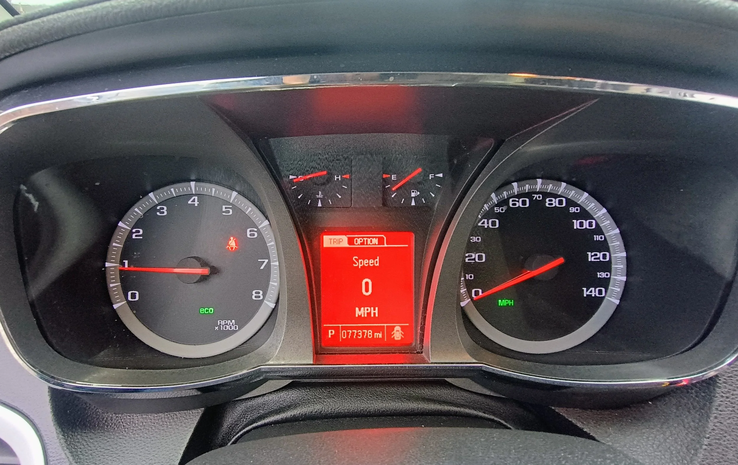 Car dashboard showing the speedometer at 0 MPH, tachometer at 1,000 RPM, fuel gauge near full, and temperature gauge slightly above cold. The digital display in the center indicates the vehicle is in park with 77,378 miles and the speed option showing zero.
