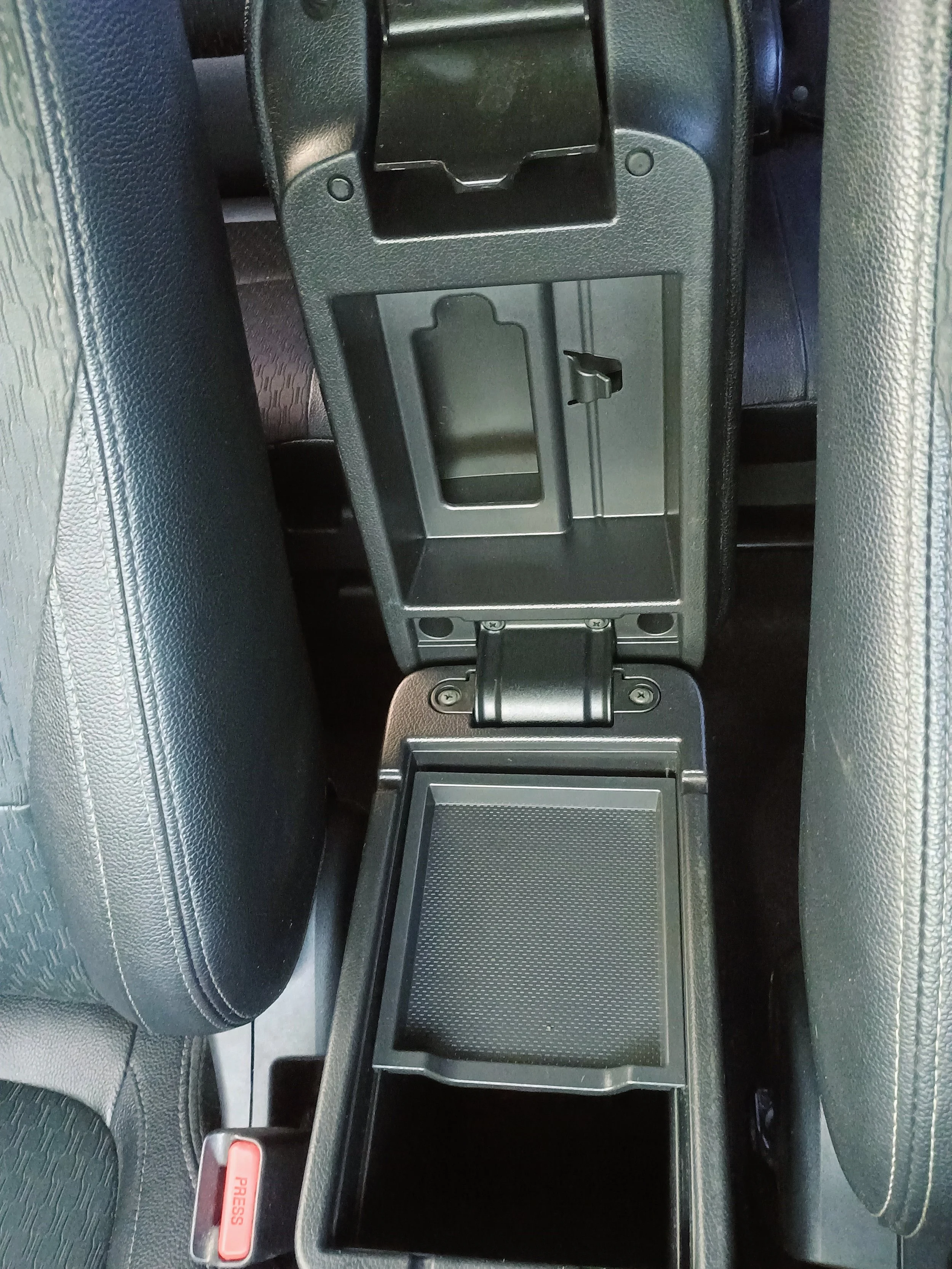 Open black car center console with storage compartment, cup holder, and seatbelt buckle on the left side.