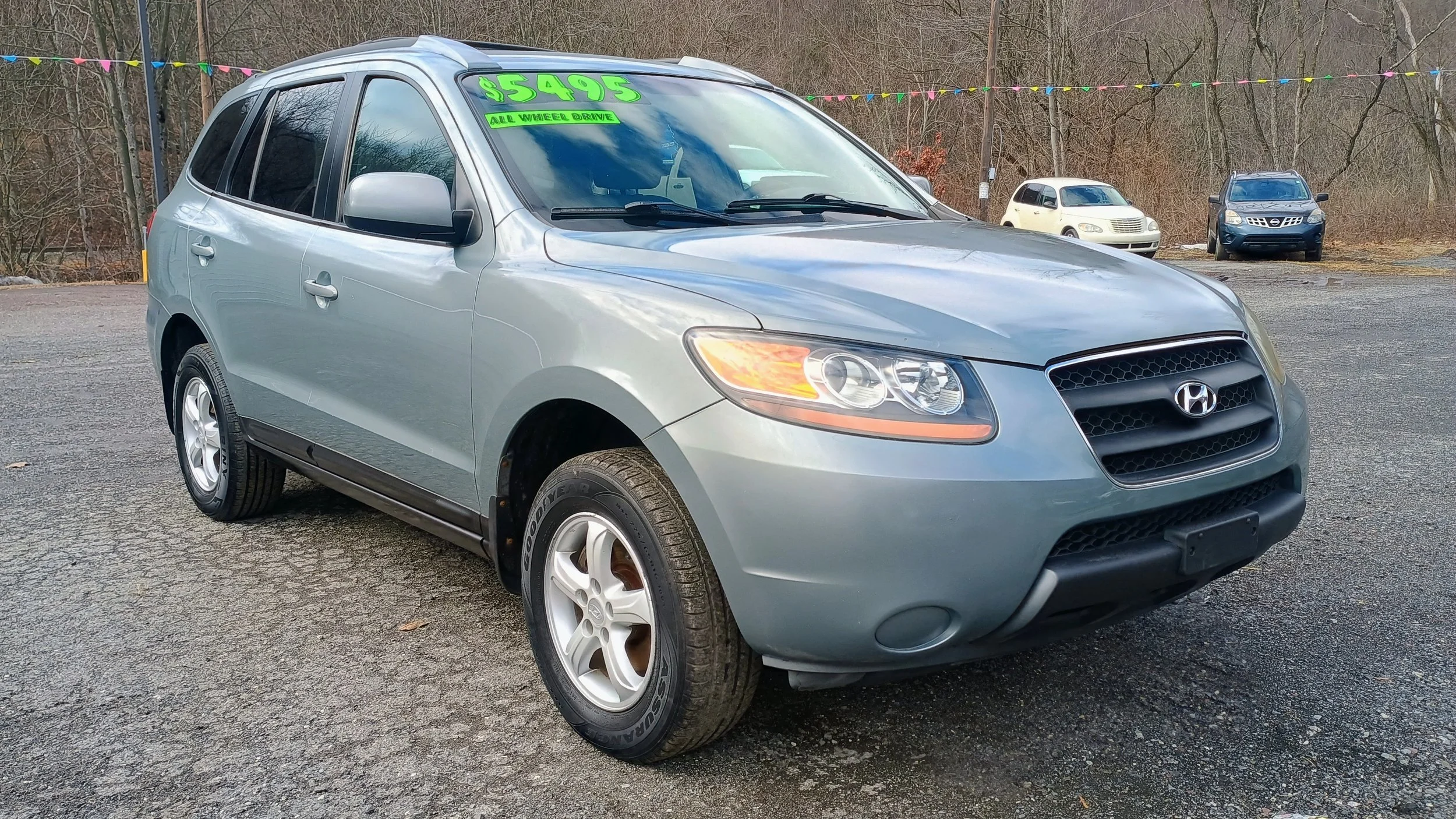 Silver Hyundai SUV for sale at a car dealership, priced at $5495, with a green sign indicating all-wheel drive