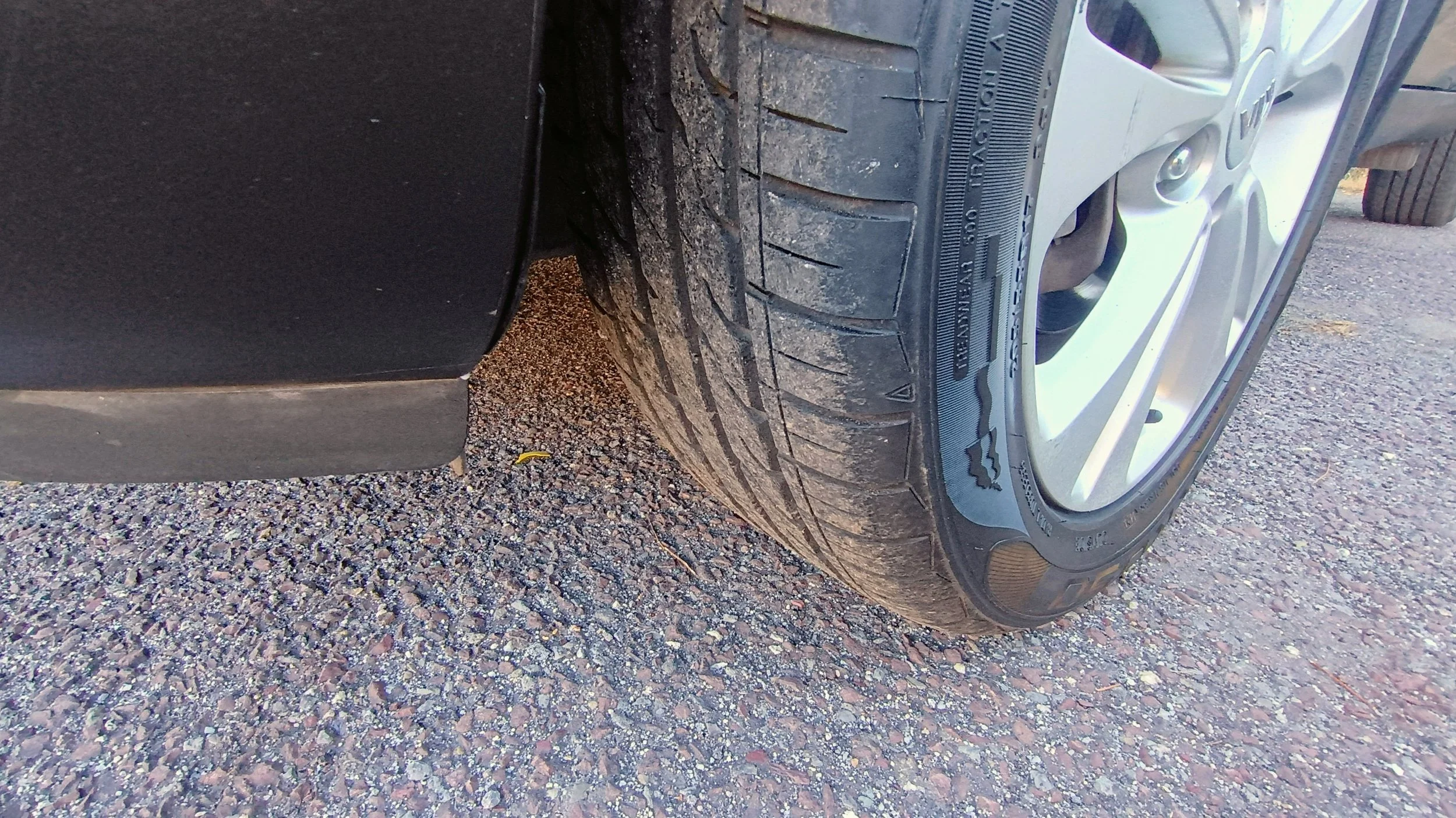 Close-up of a car tire on gravel ground, showing the tread pattern and sidewall details.