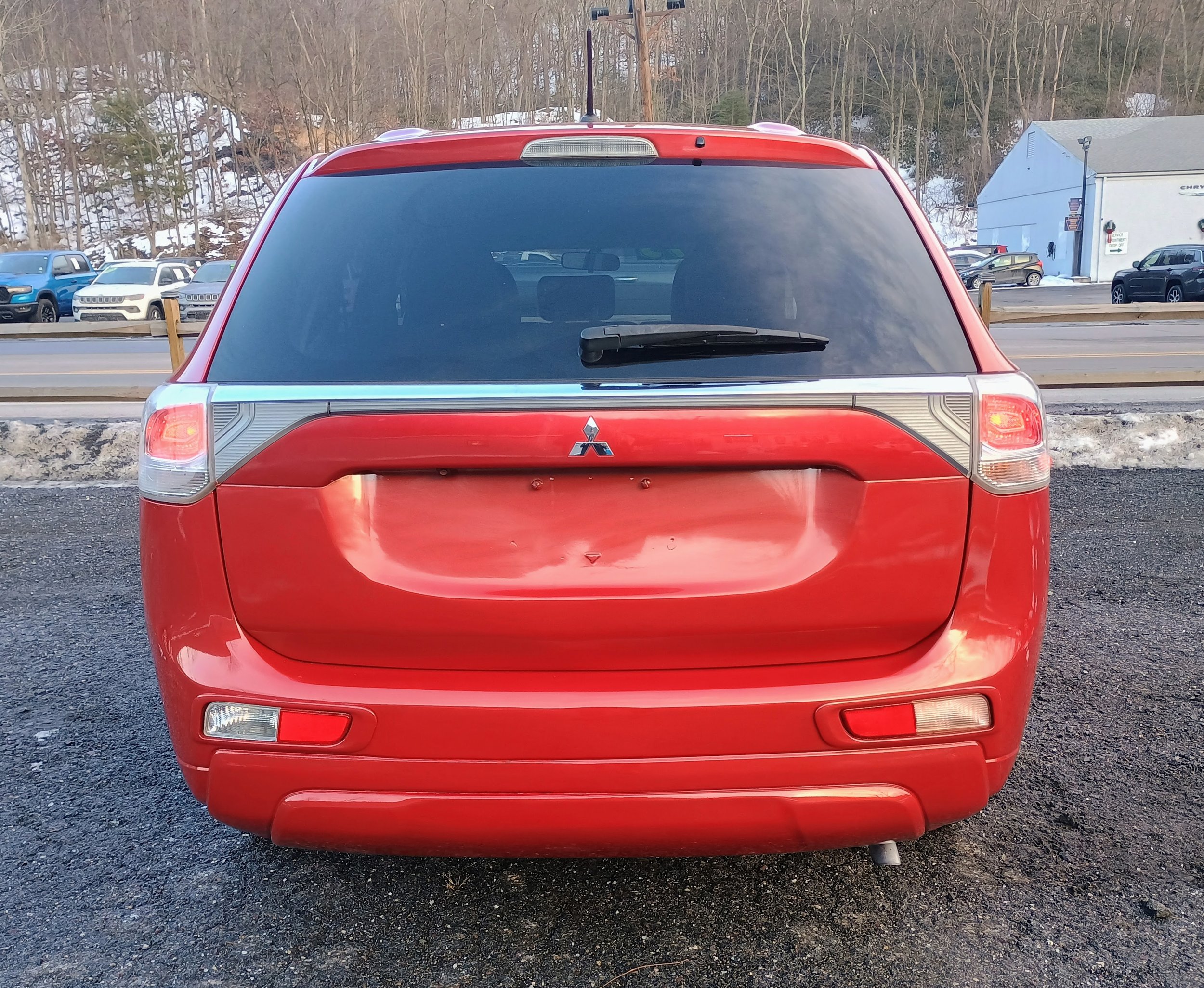 Red SUV parked outdoors with a rear view, including a black rear windshield wiper and the Mitsubishi logo on the back.