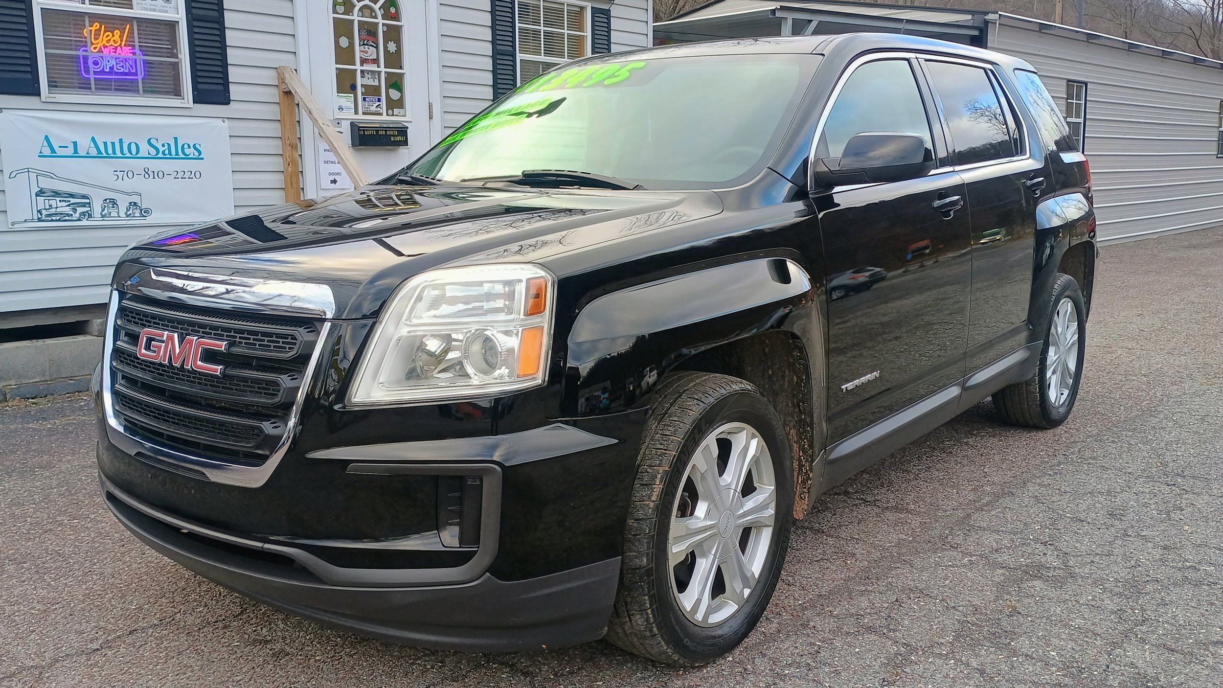 Black GMC Terrain SUV parked in front of a building with signs for auto sales and open hours.