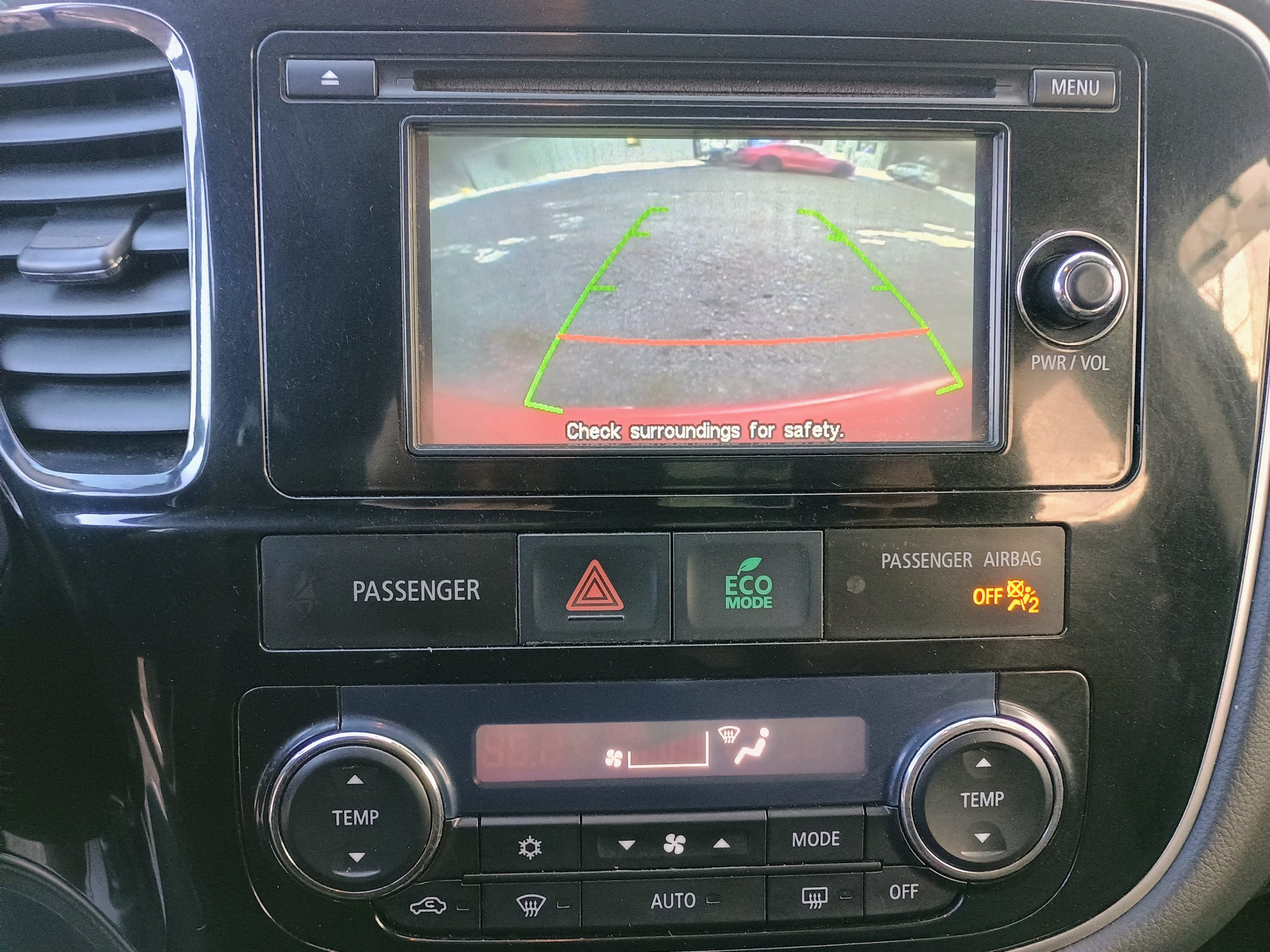 Car's dashboard showing a rearview camera display with parking guidelines and a message to check surroundings for safety.