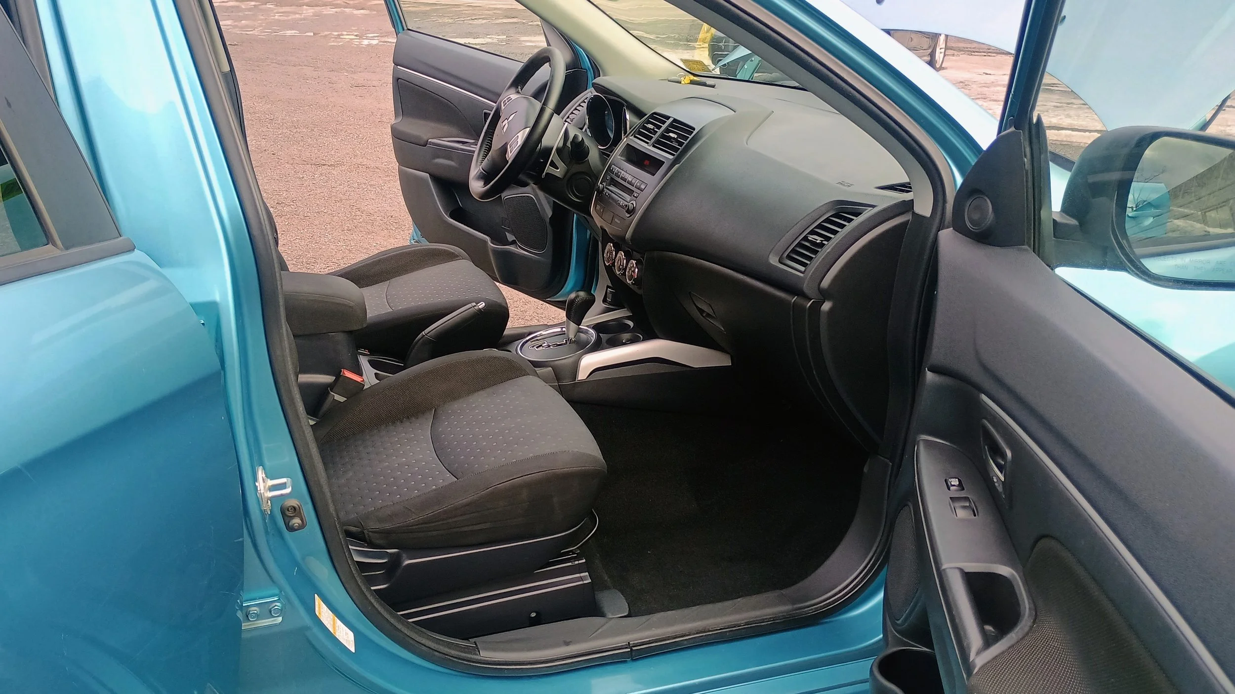The interior of a blue vehicle showing the driver's seat, passenger seat, dashboard, steering wheel, gear shift, and door panel with window controls.