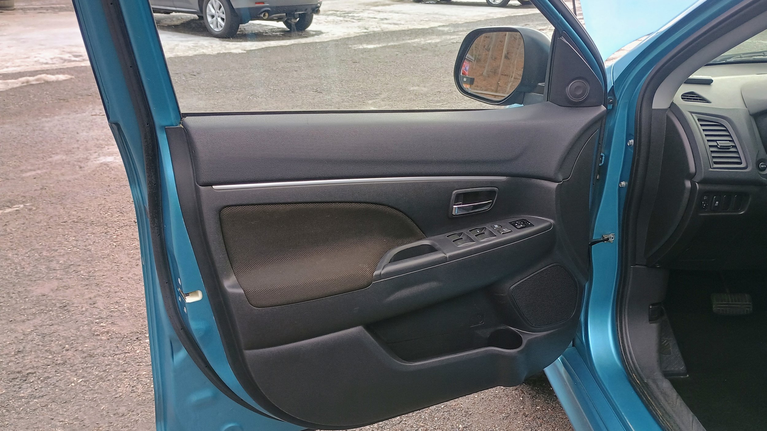 The image shows the interior of a blue car, focusing on the driver's side door panel which contains control buttons, a speaker, and a door handle.