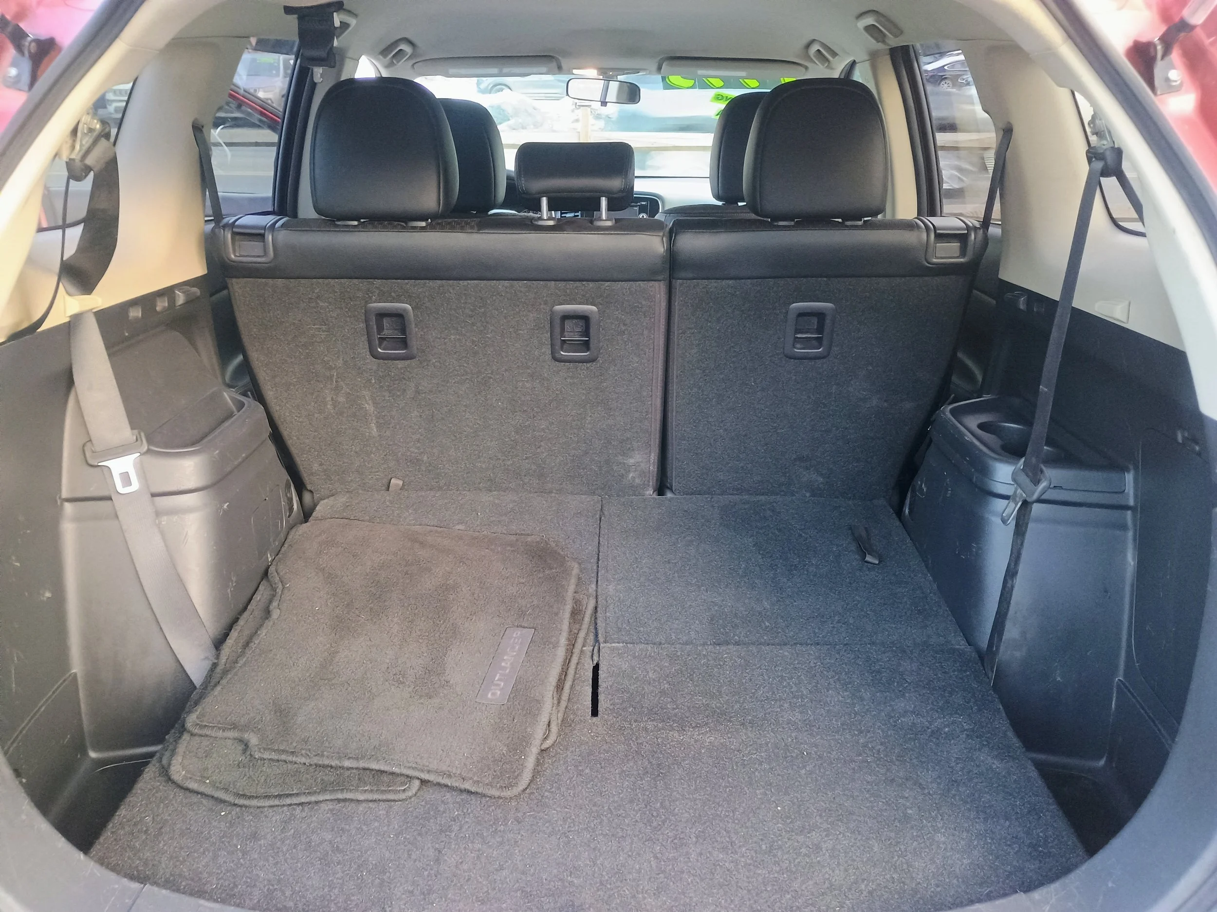 Interior of an SUV showing the cargo area with folded rear seats, a car floor mat, and storage compartments on both sides.