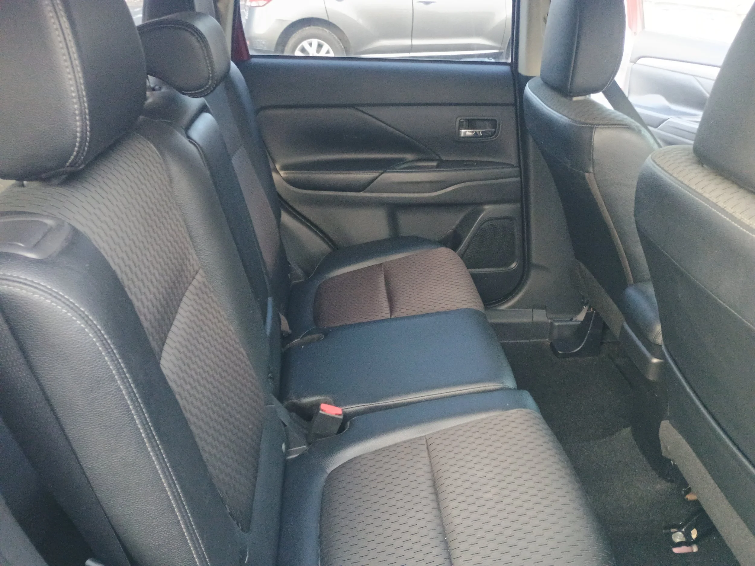 Rear interior of a vehicle, showing black and brown seats, black door panel, and window with a vehicle outside.