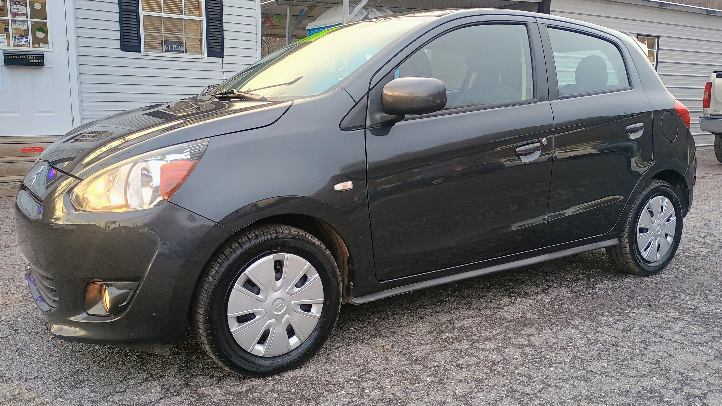 Black compact hatchback car parked on a gravel surface near a building with white siding and black window shutters.