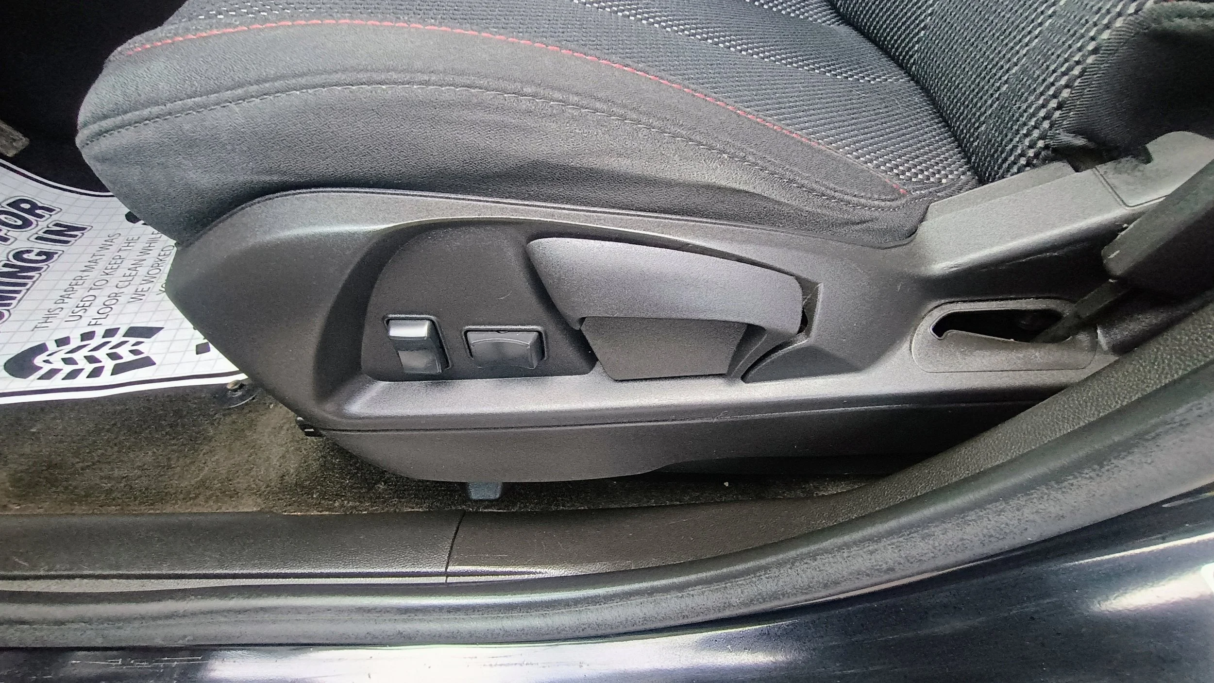 Close-up of a car seat's side with manual and electronic adjustment levers and a seat belt buckle.
