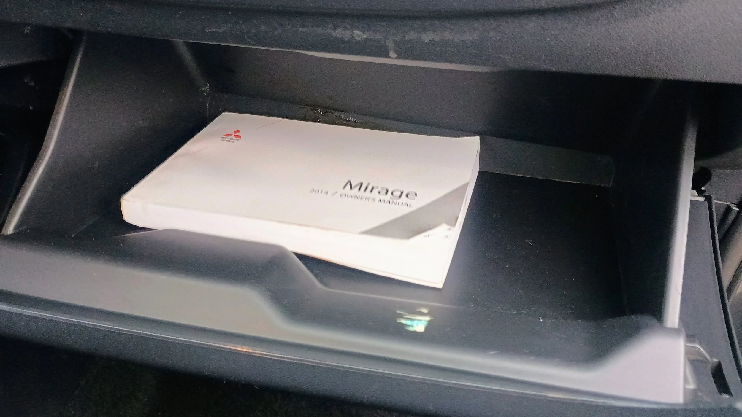 Open glove compartment in a vehicle with a Miragge owner manual inside.