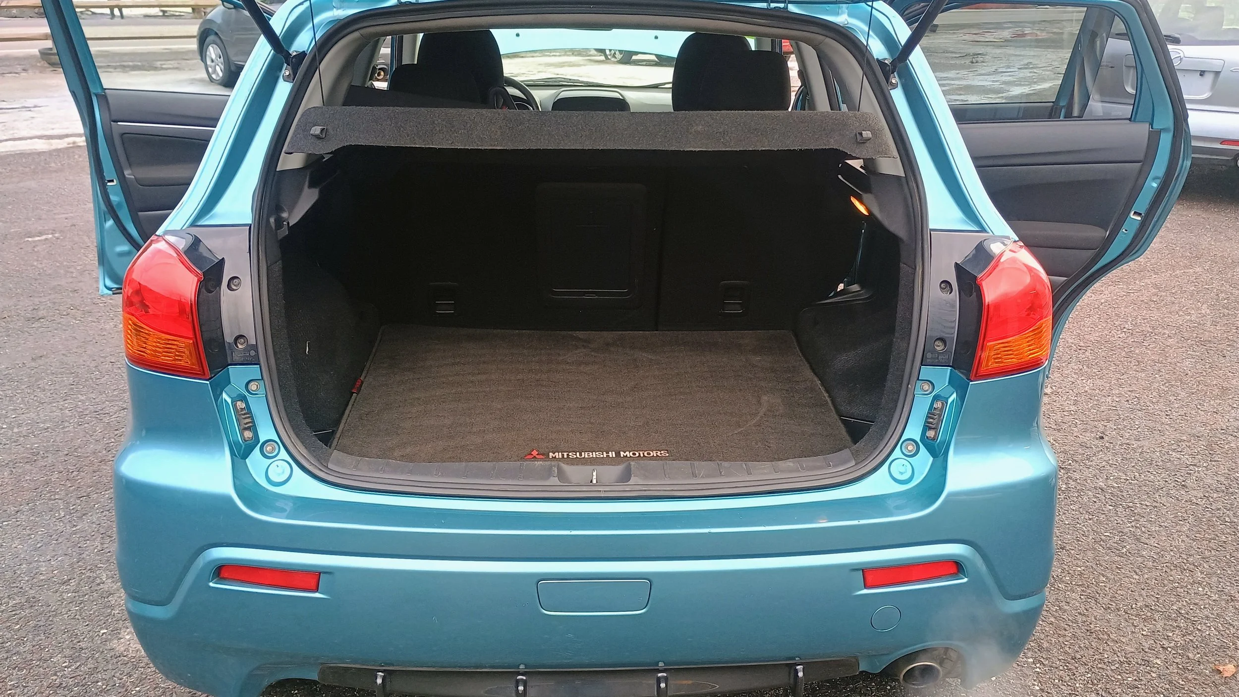 Open trunk of a blue hatchback car showing interior space with black seats and a cargo area with a Mitsubishi Motors mat.