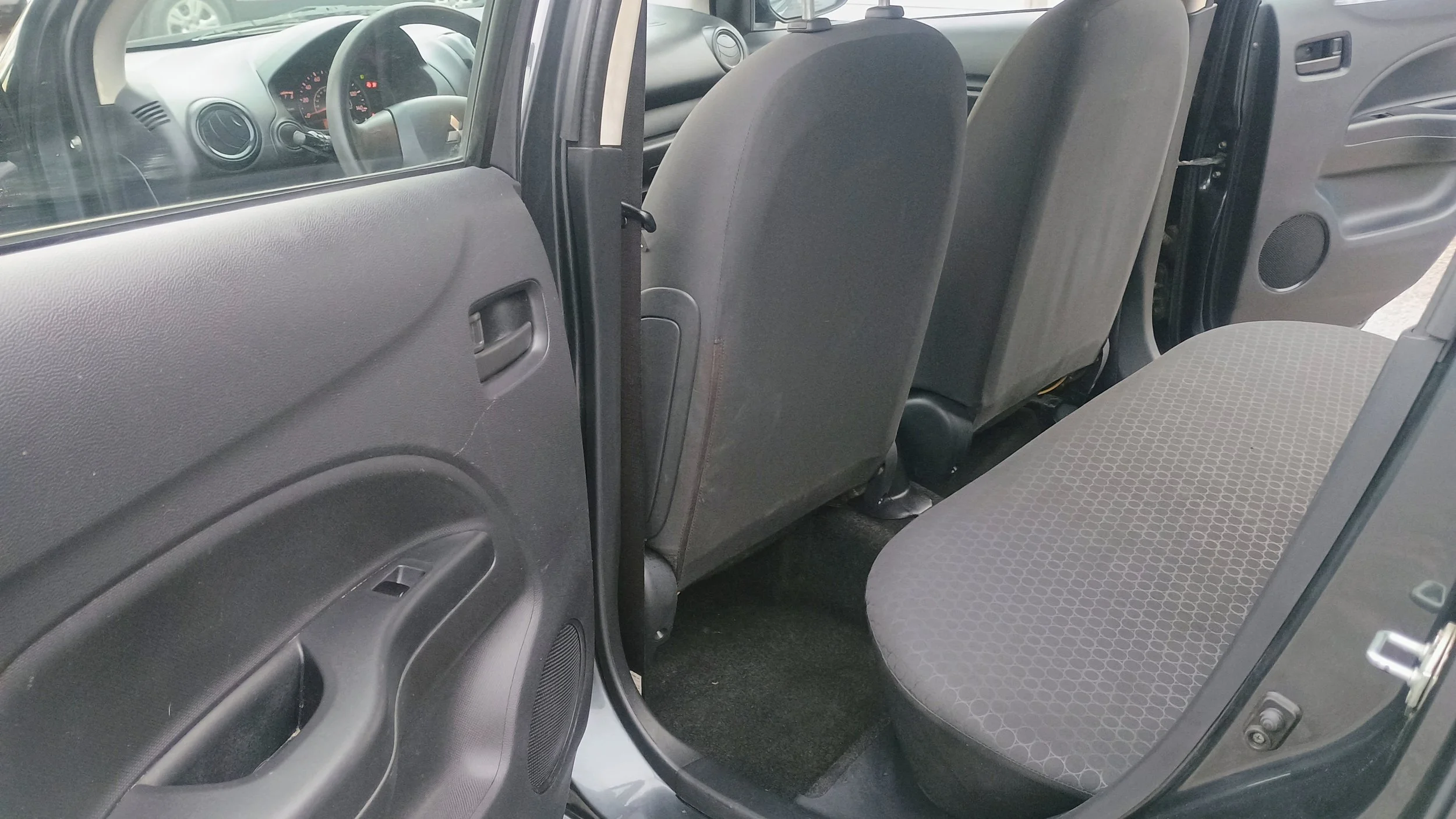 Interior of a compact car showing the back seat, front seats, steering wheel, dashboard, and driver side door panel.