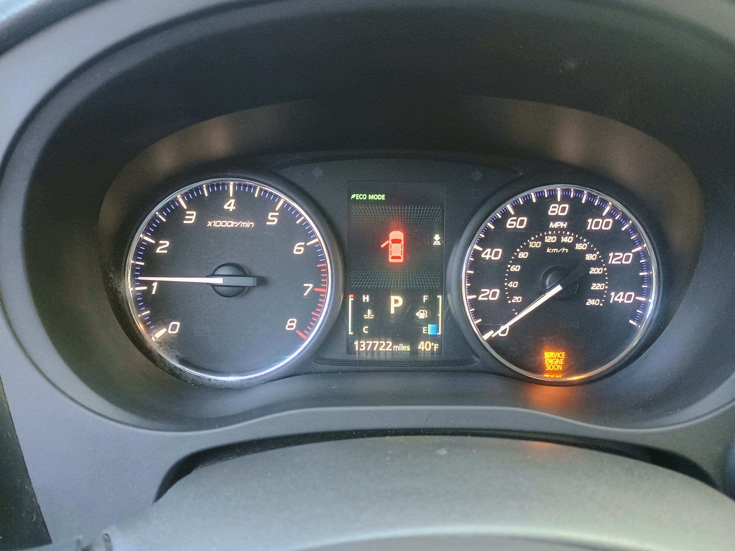 Car dashboard showing the speedometer at 0 mph, tachometer at 1,000 rpm, fuel gauge on F, temperature at C, and warning lights including a red door indicator, service engine soon, and a message indicating service is needed soon. The odometer reads 137,722 miles, and the outside temperature is 40°F.