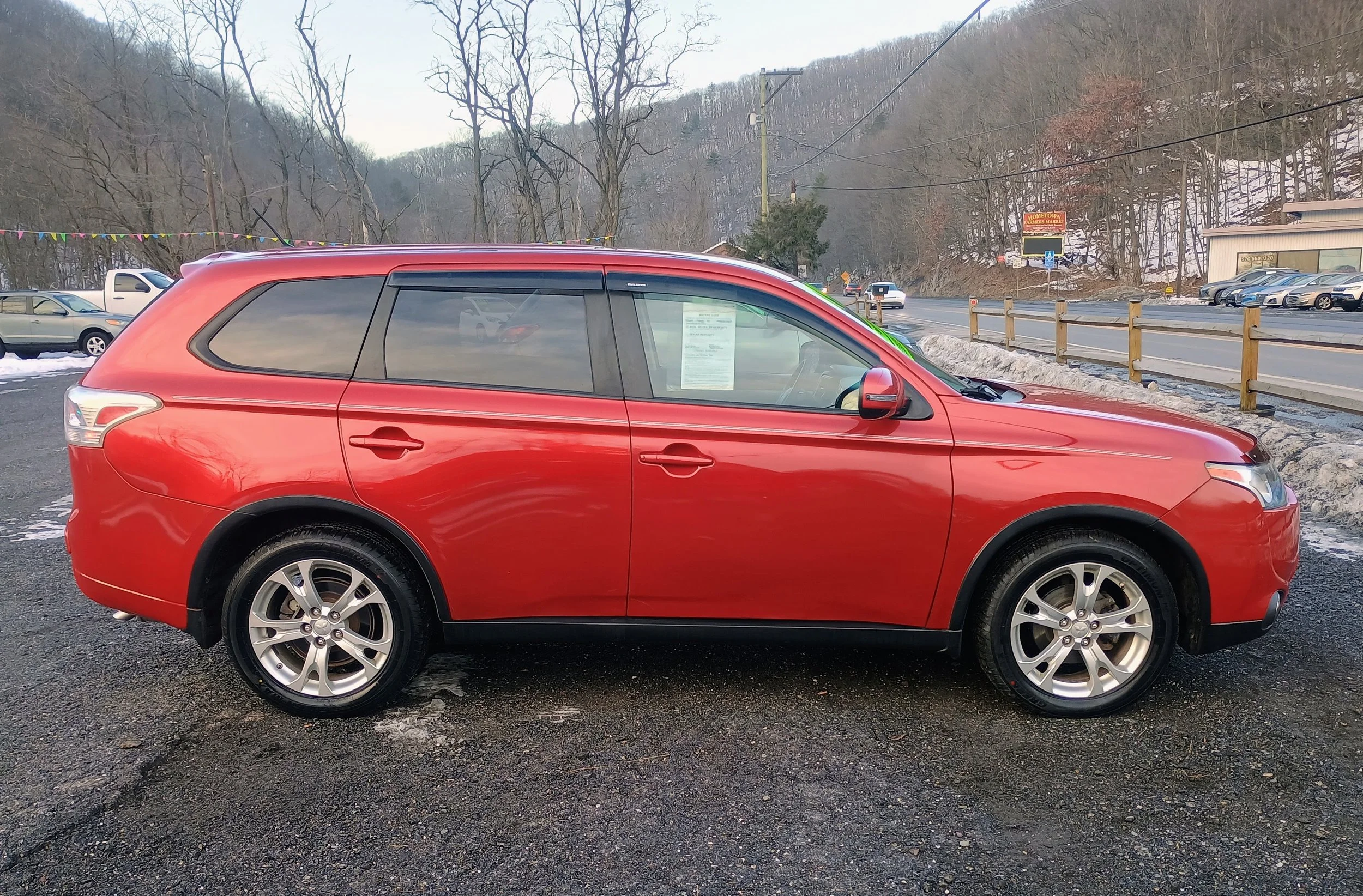 Red SUV parked in a lot with trees and a road in the background.