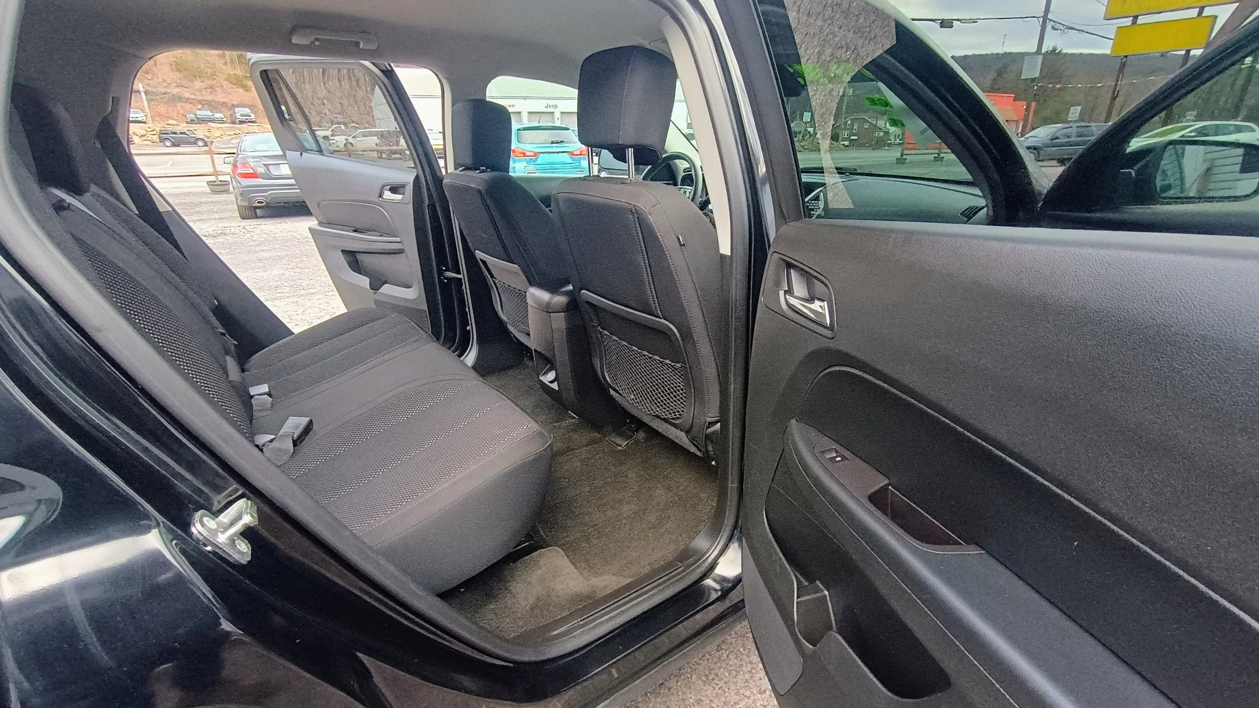 The interior of a black SUV with the rear passenger door open, showing the back seat area with gray cloth seats and front seats, floor, and rear side door panel.