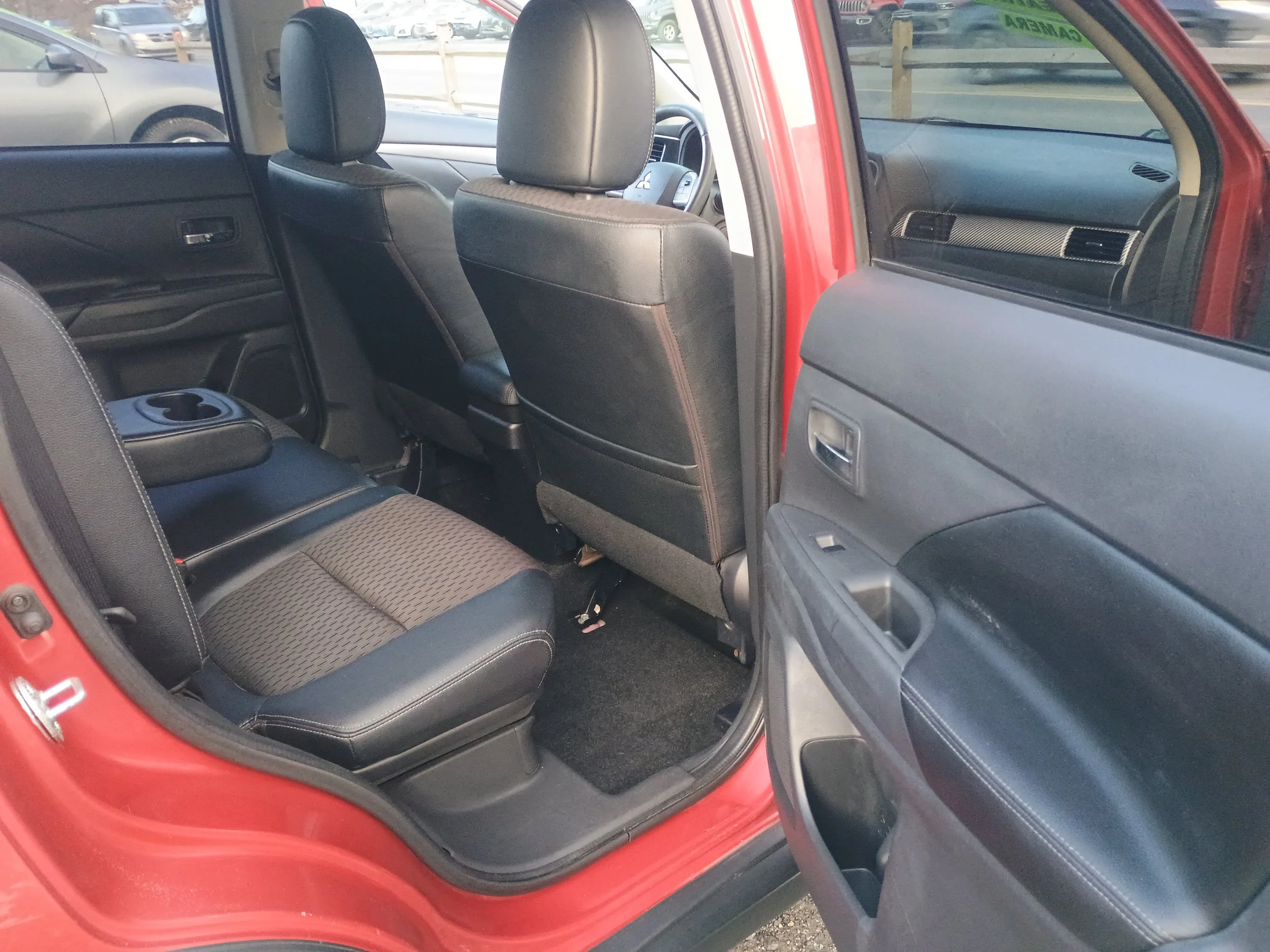 Interior of a red truck showing black fabric seats, back of front seats, and the open rear passenger door.