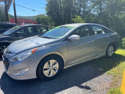 Silver sedan parked on a gravel lot with other cars and green trees in the background.