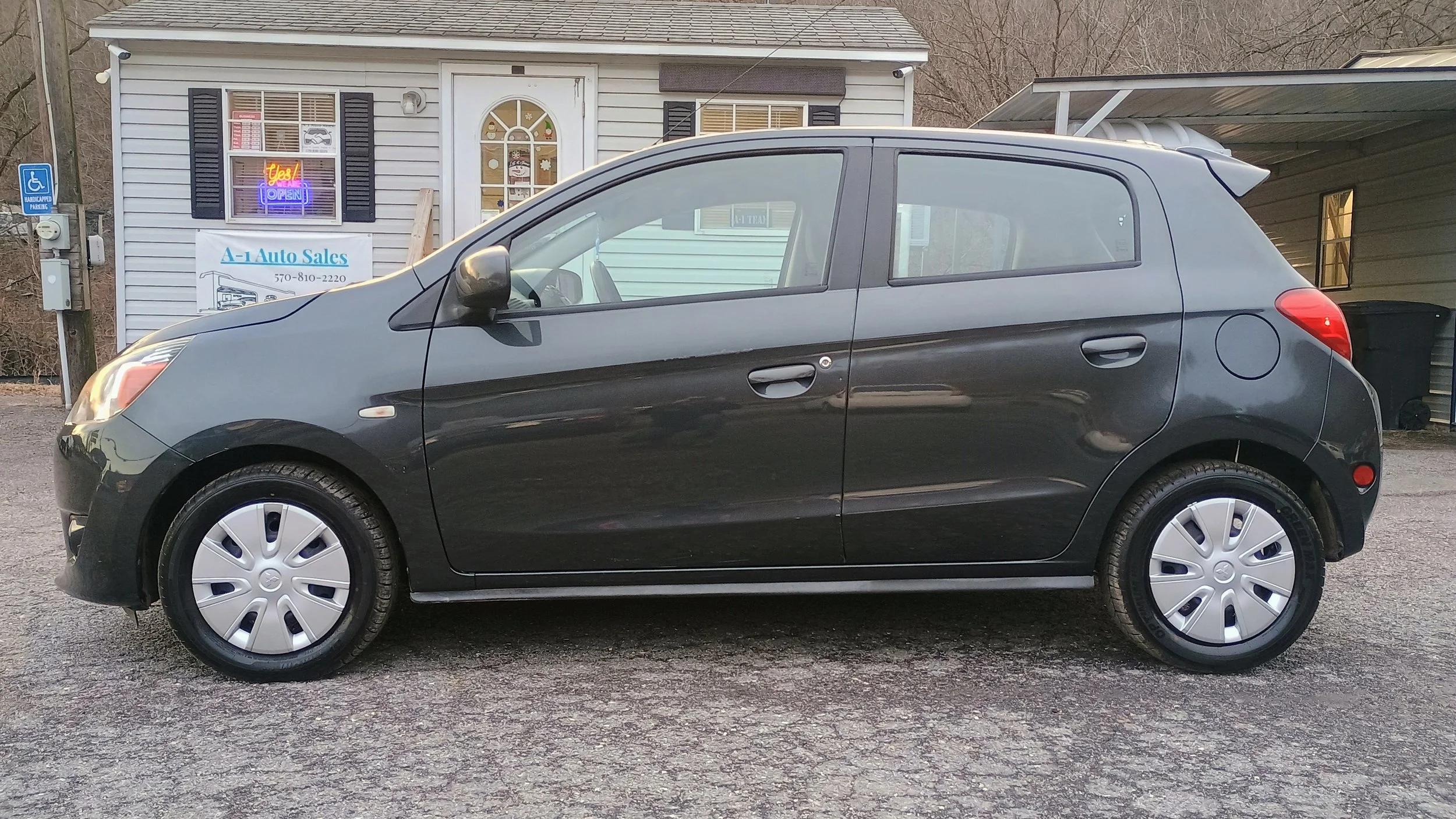 A black hatchback car parked outside a house with a sign for A-1 Auto Sales in the background
