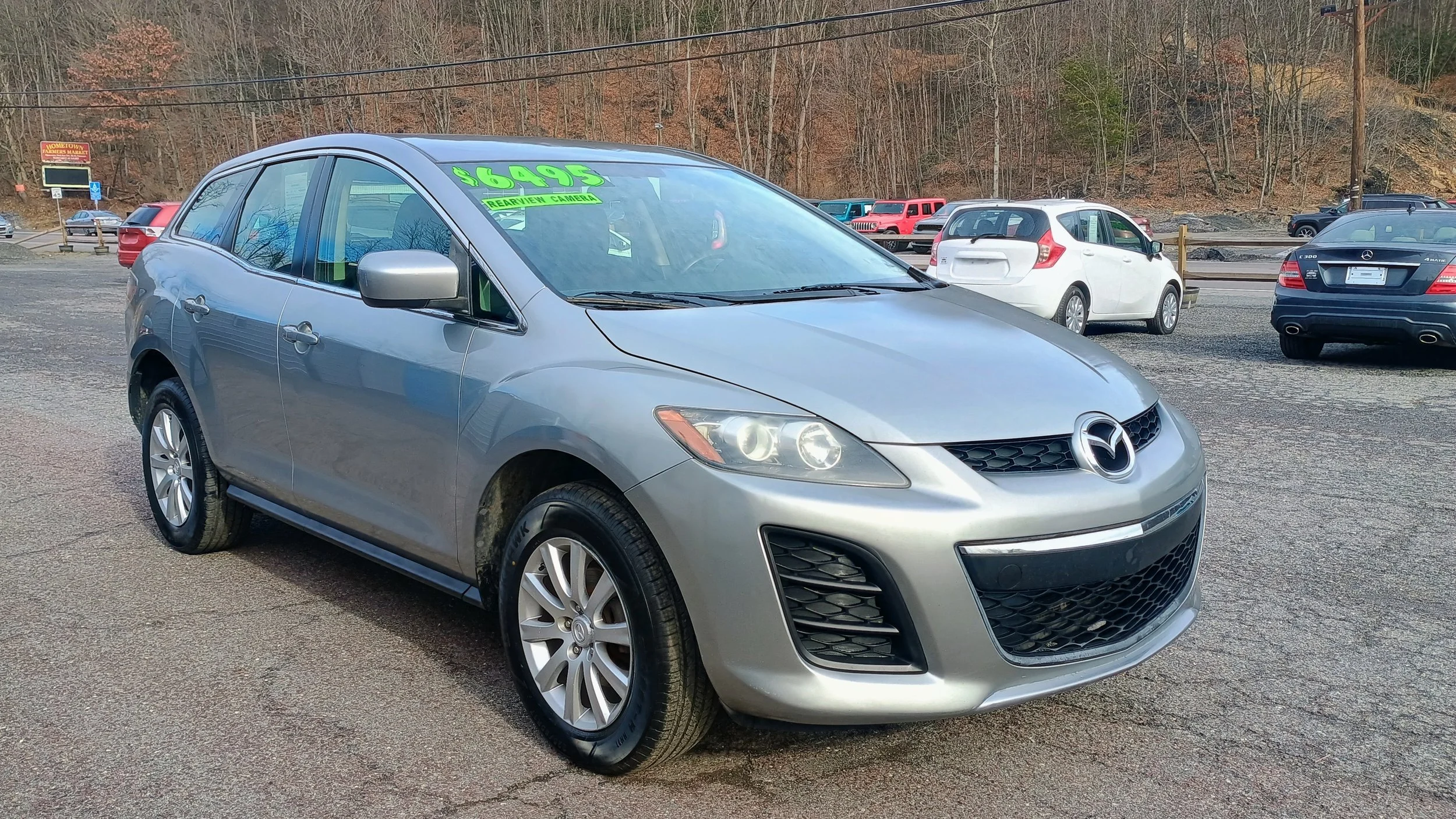 Silver Mazda hatchback car for sale in a used car lot with a green price sign on the windshield.